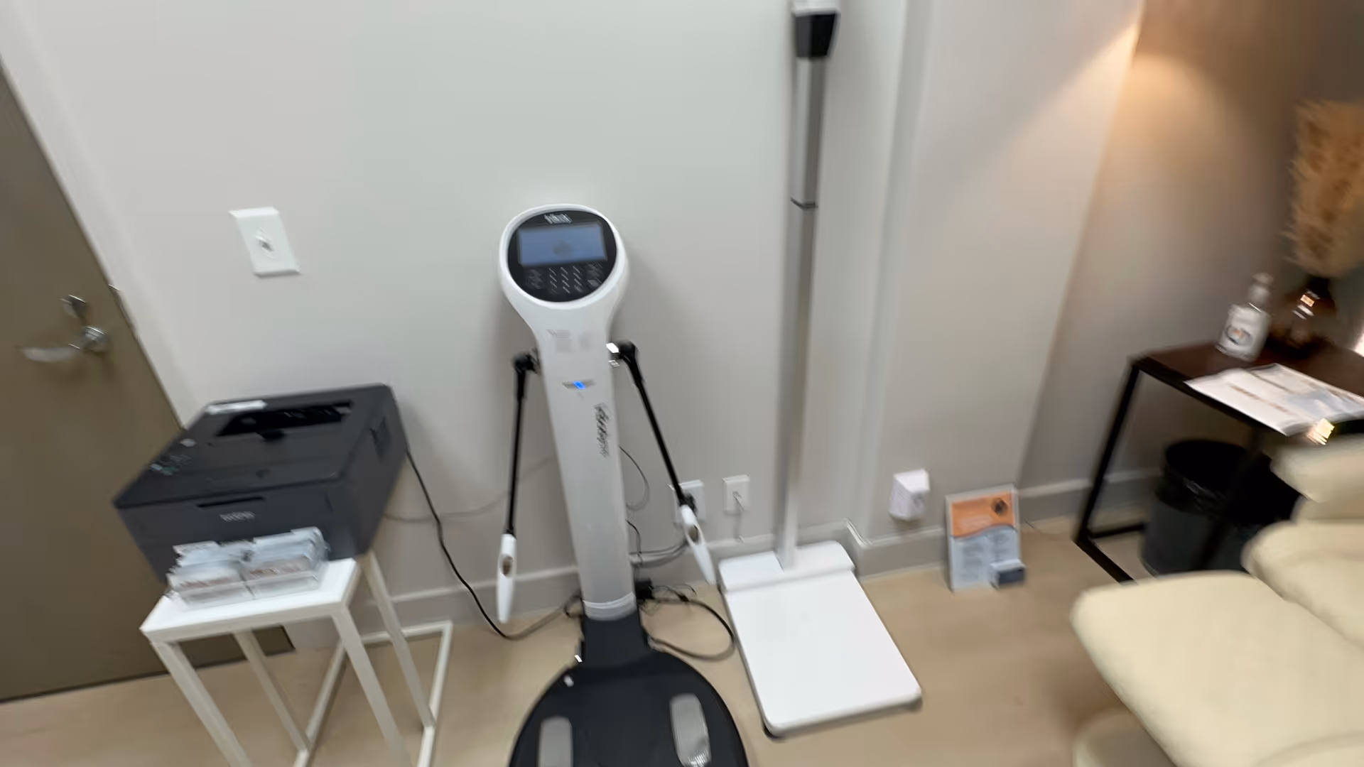 Medical equipment corner features a digital scale, printer, and seating in a clean room.