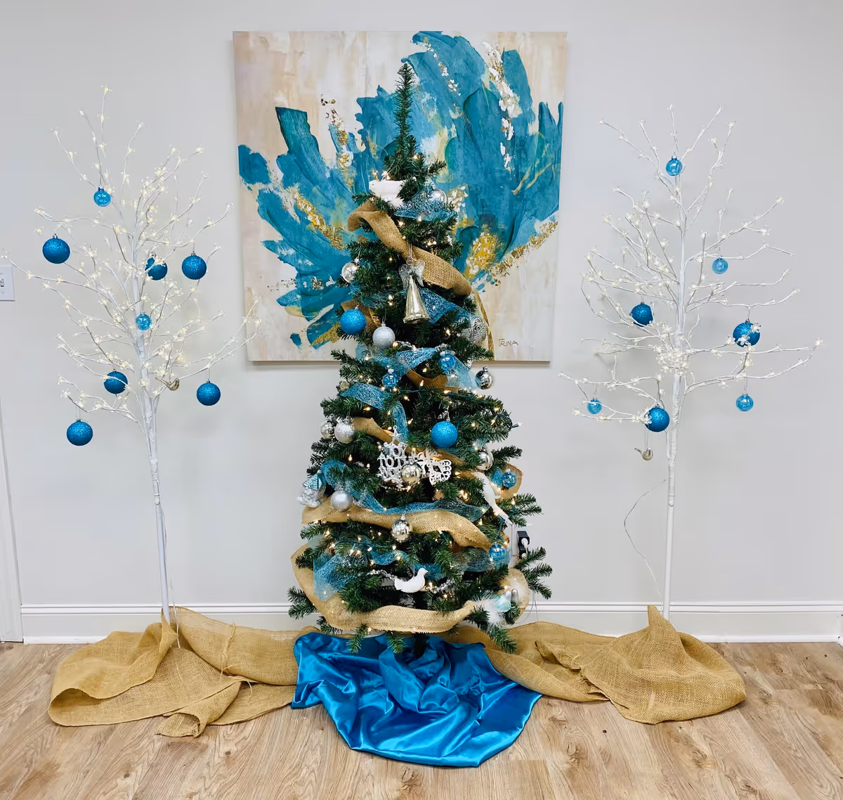 Decorated Christmas tree with blue ornaments flanked by white, lighted trees indoors