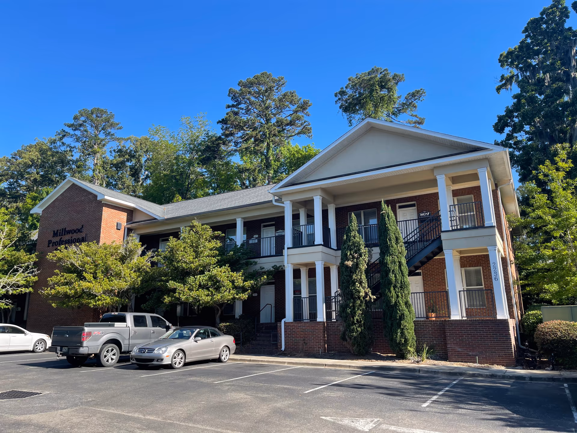 Two-story brick senior living building with a parking lot and trees.