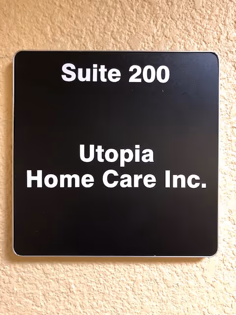 Black wall plaque reading Suite 200 and Utopia Home Care Inc. on beige wall.