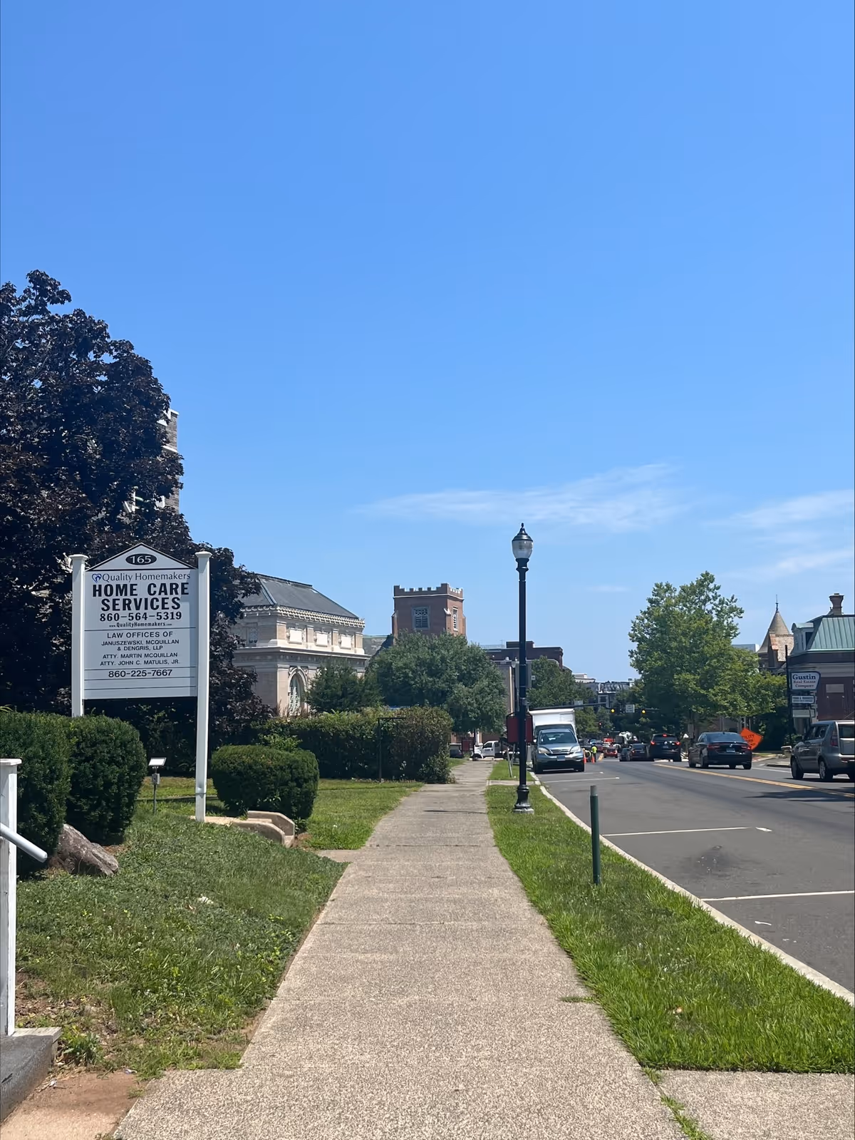 Sidewalk view of a street with a Quality Homemakers Home Care Services sign.