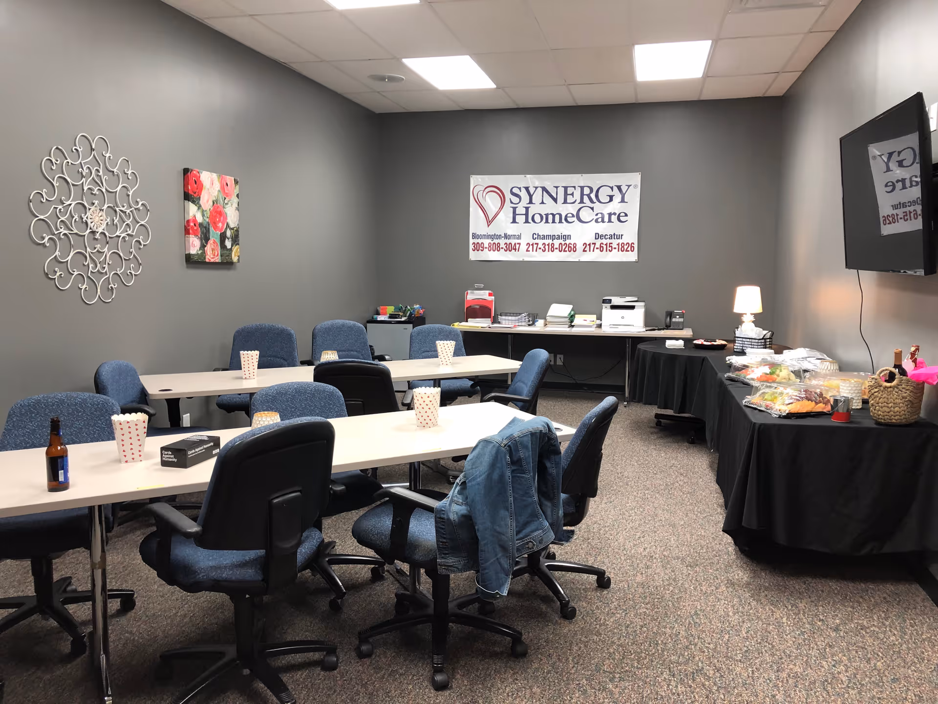 Meeting room in a Synergy HomeCare facility with conference tables, blue chairs, and a snack buffet.