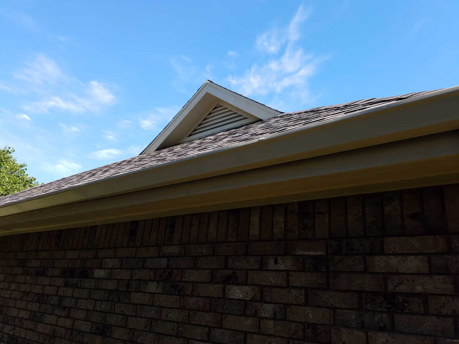 Brick exterior wall with sloped roof and triangular vent under blue sky.