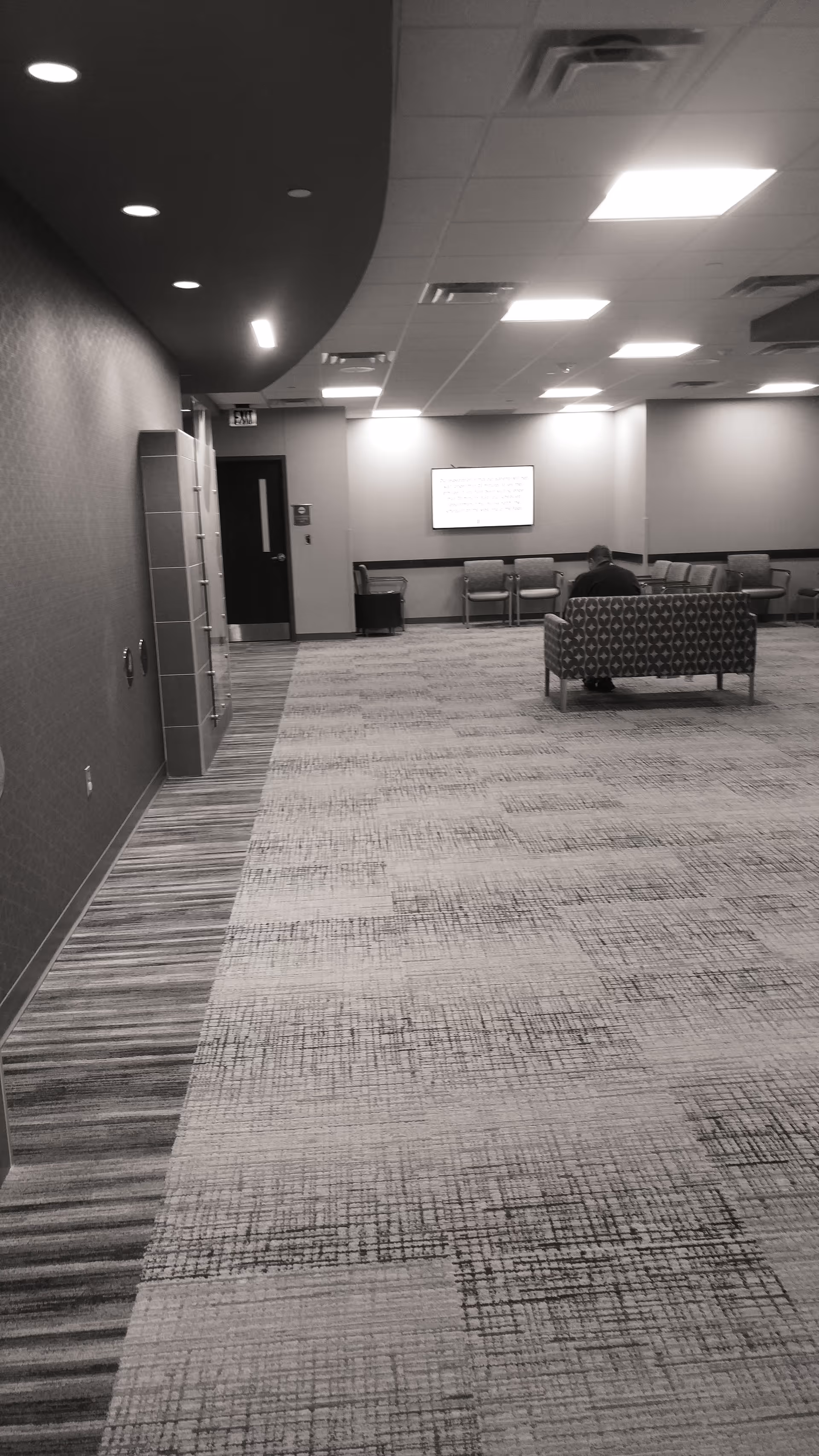 Dimly lit indoor corridor with lounge seating and one person seated.