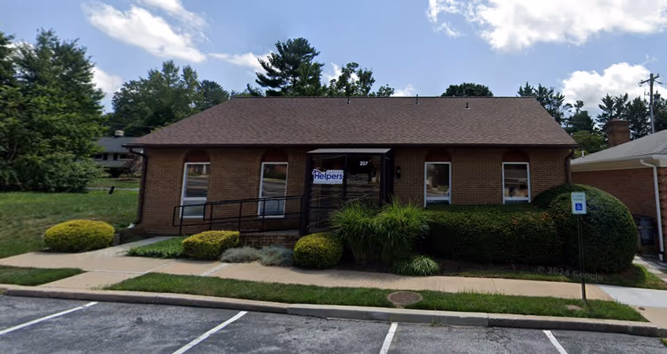 Single-story brick Senior Helpers building with glass entry, manicured shrubs, and a paved sidewalk.