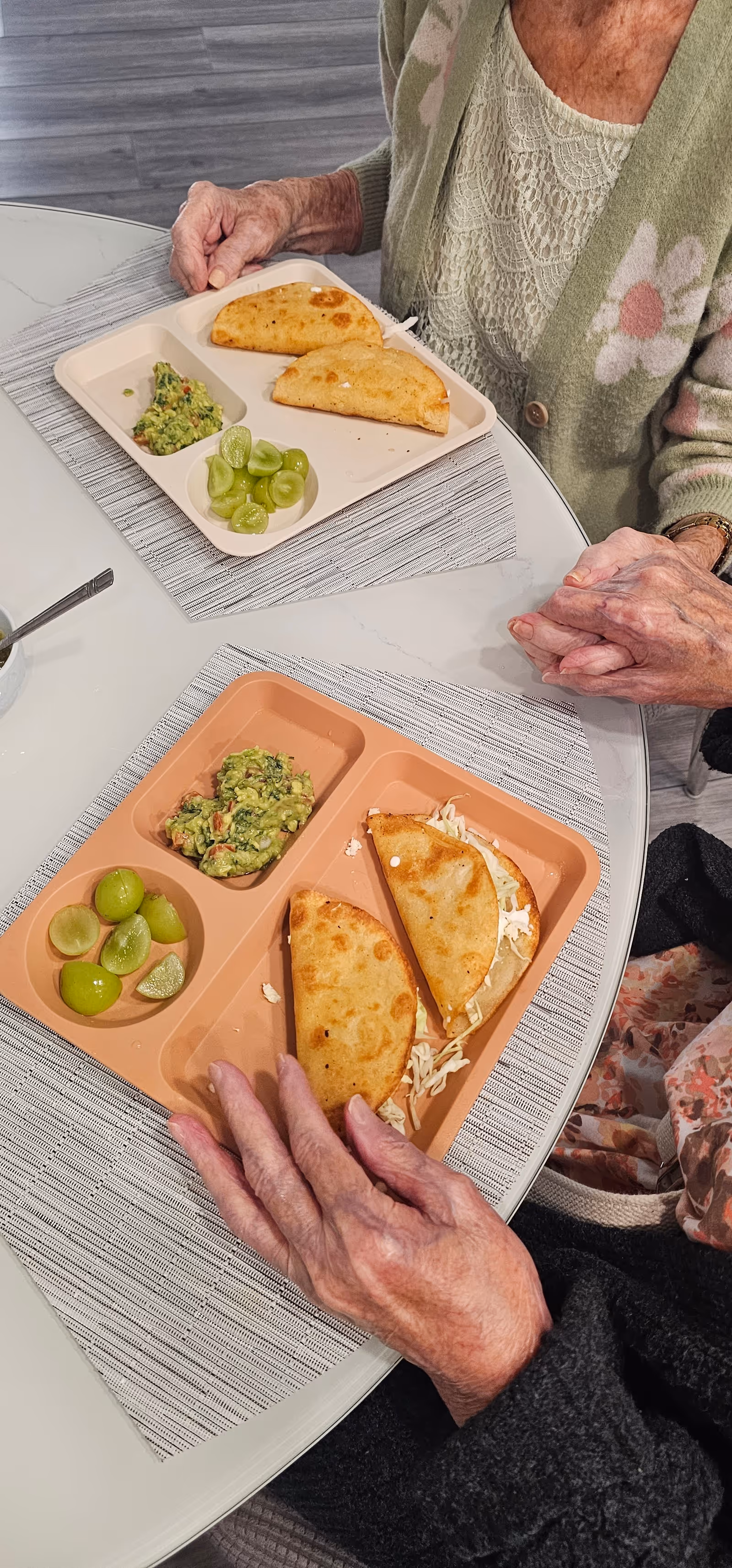 Elderly person seated at a dining table with divided trays of quesadillas and lime wedges.