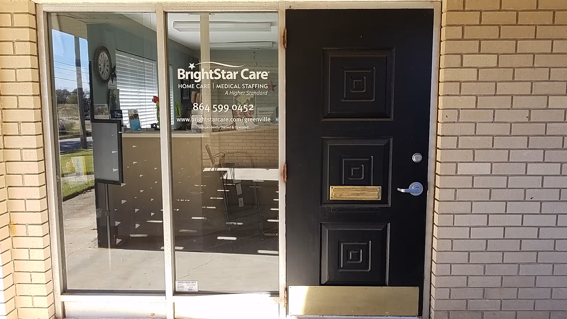 Brick building entrance with glass door displaying BrightStar Care logo and contact info