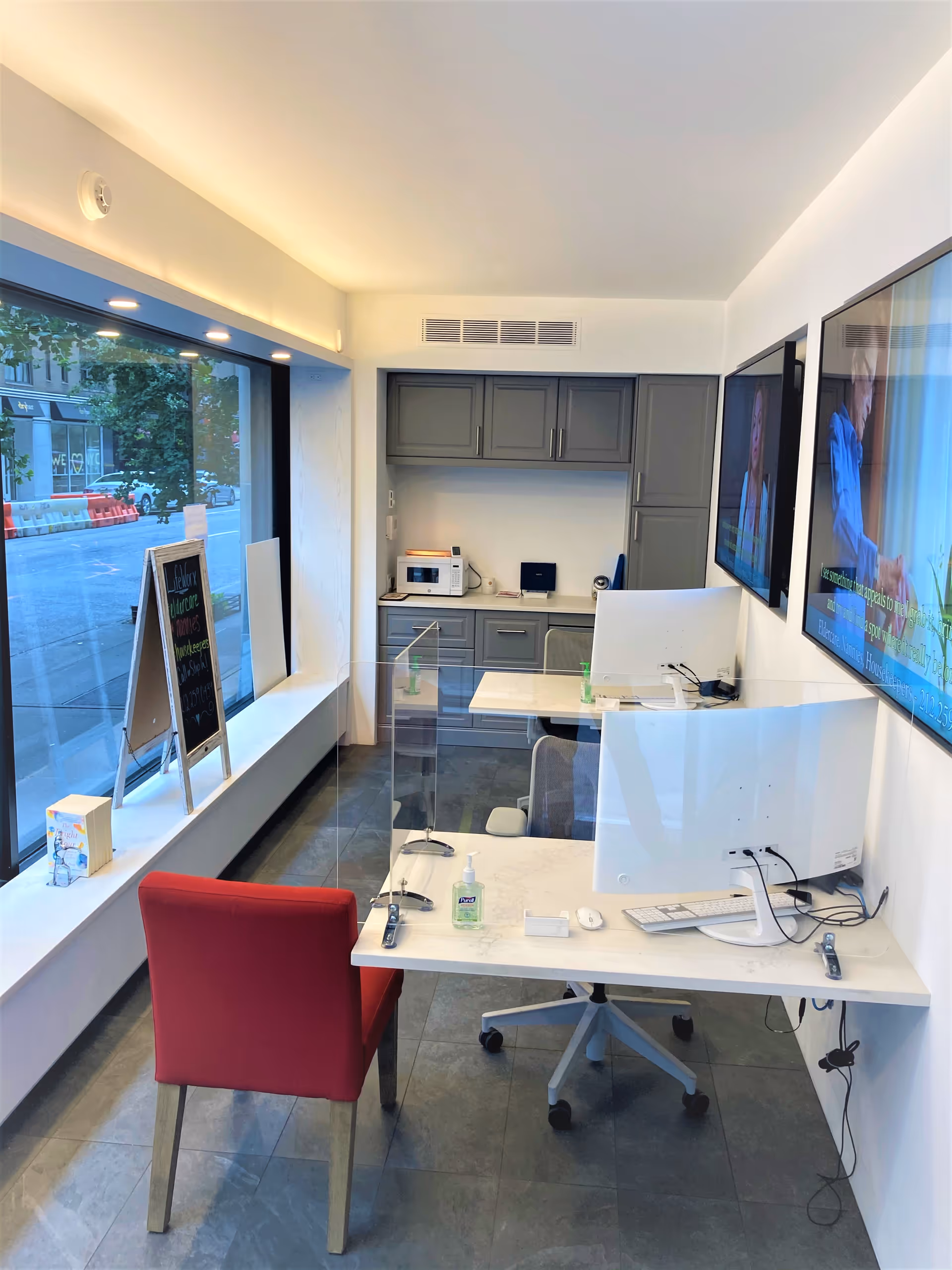 Modern reception area with white desk, glass divider, monitor, and gray cabinetry.