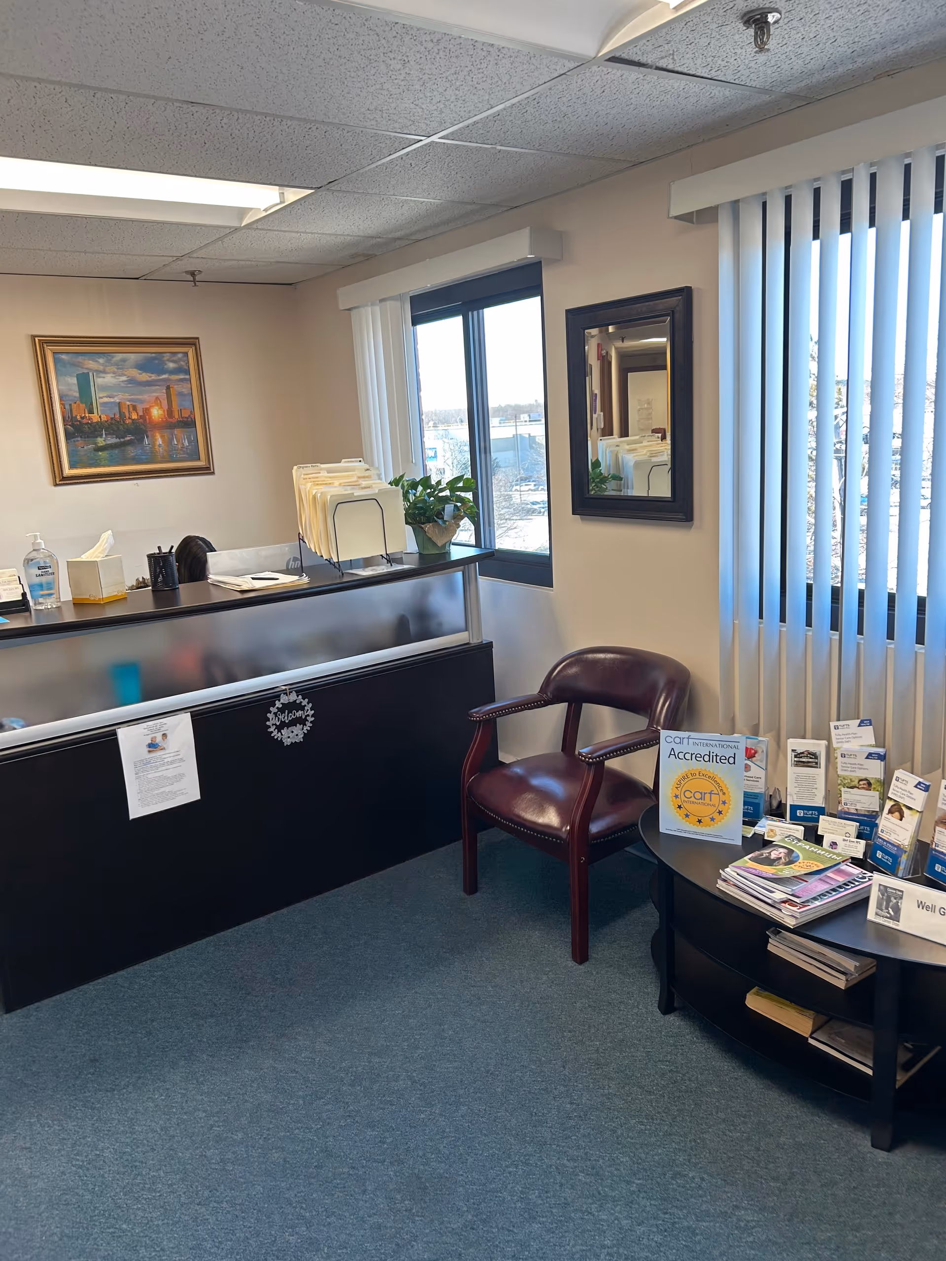 Reception desk with files, a burgundy chair, brochures, and large windows.