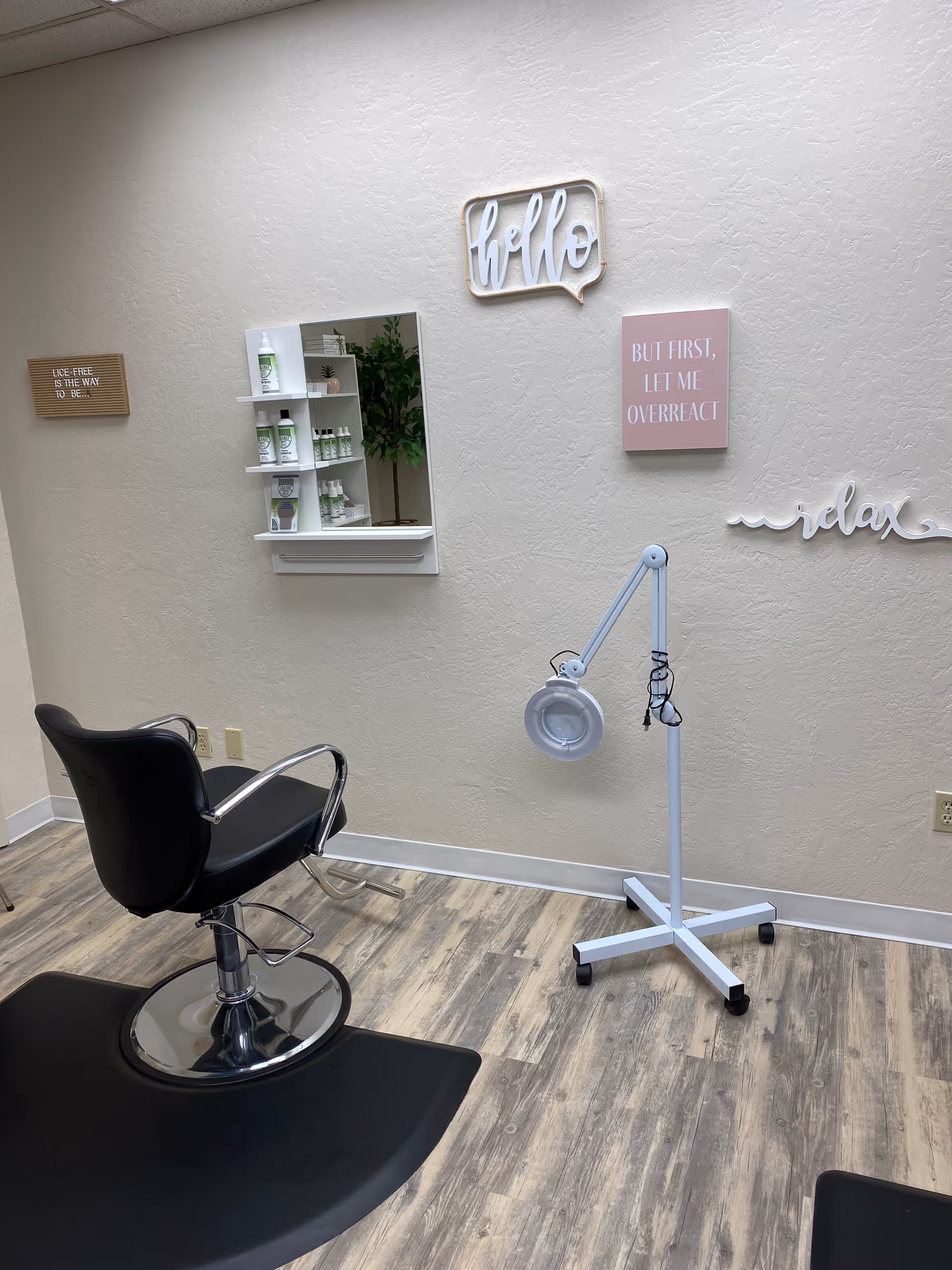 Small interior salon room with a black styling chair, magnifying lamp, and decorative wall art.