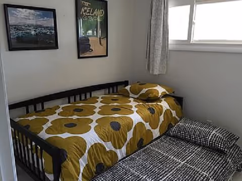 Small bedroom with a twin bed, yellow floral bedding, wall posters, and a window.