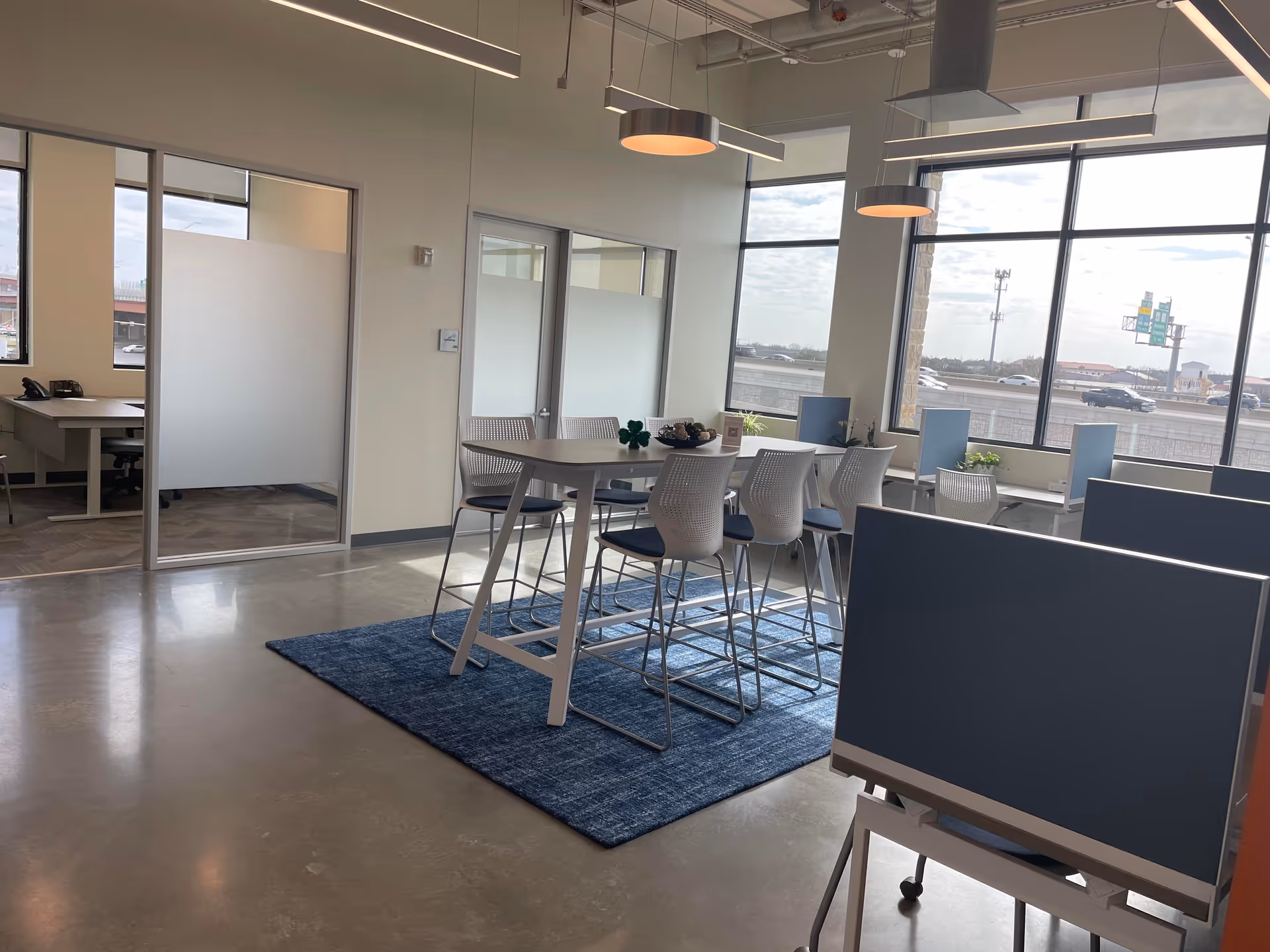 Modern indoor communal area with high tables, stools, and large windows.