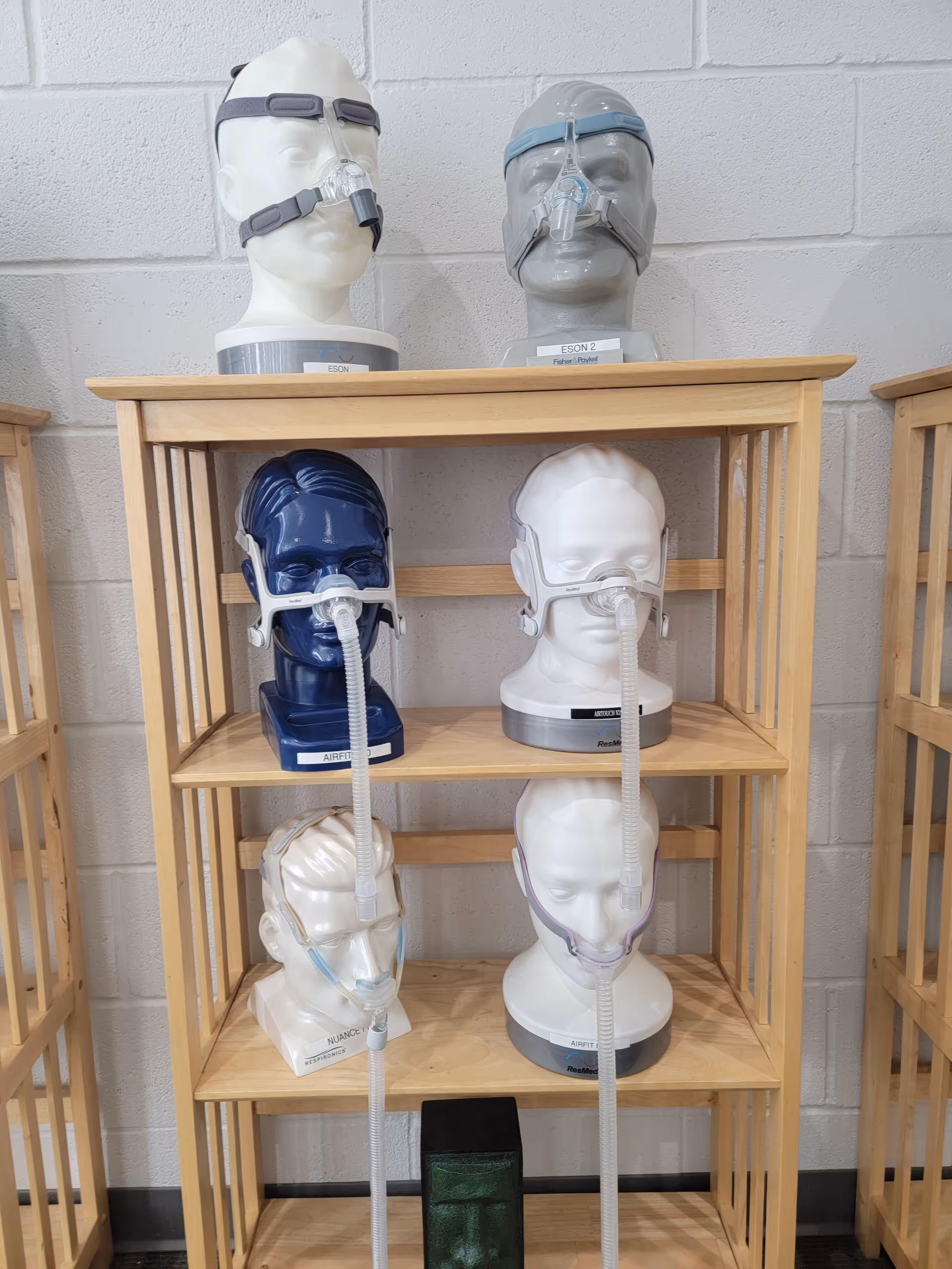 Row of CPAP masks on shelves with mannequin heads against a brick wall