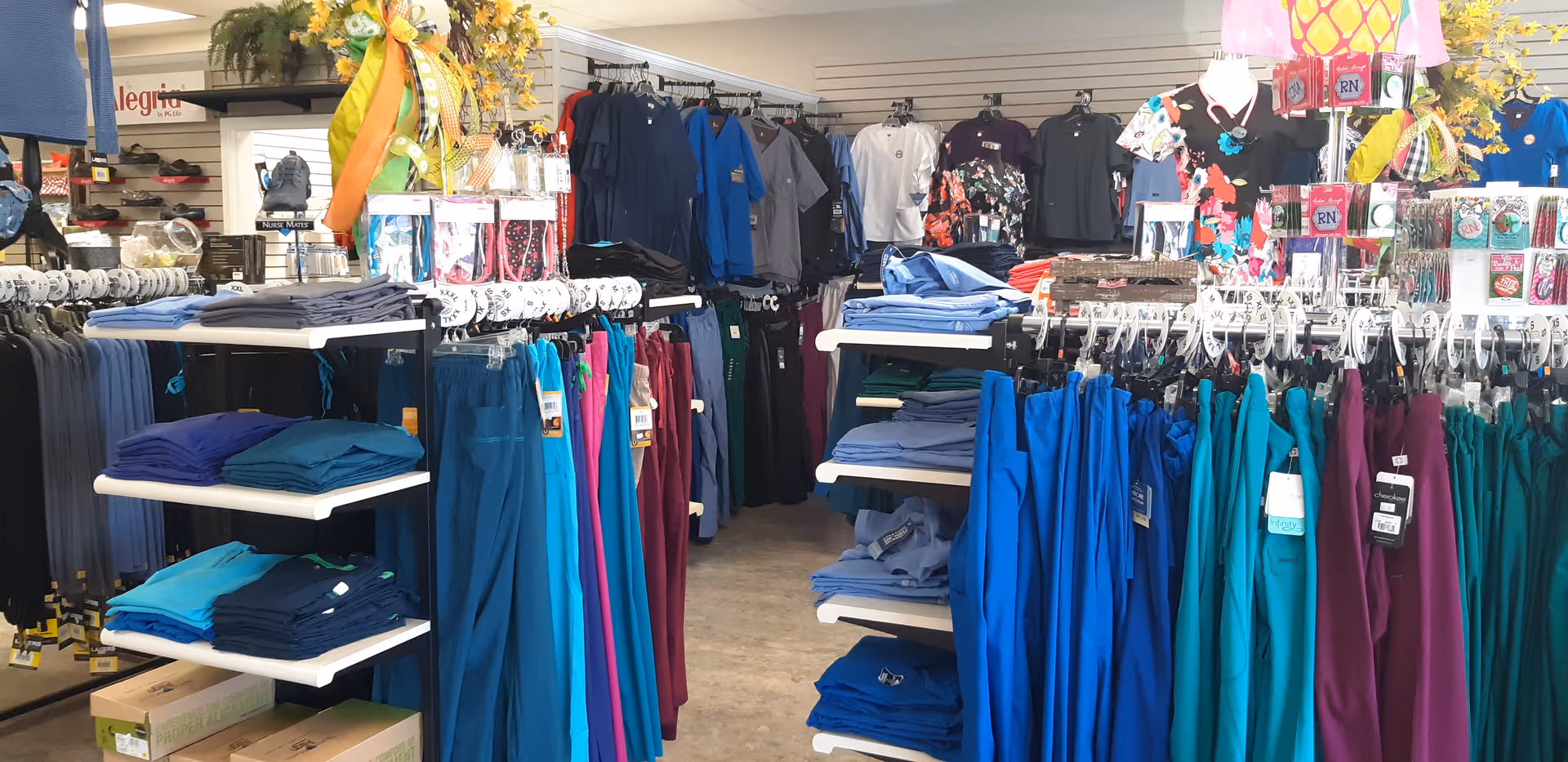 Store interior with racks of colorful scrubs and folded clothing on shelves.