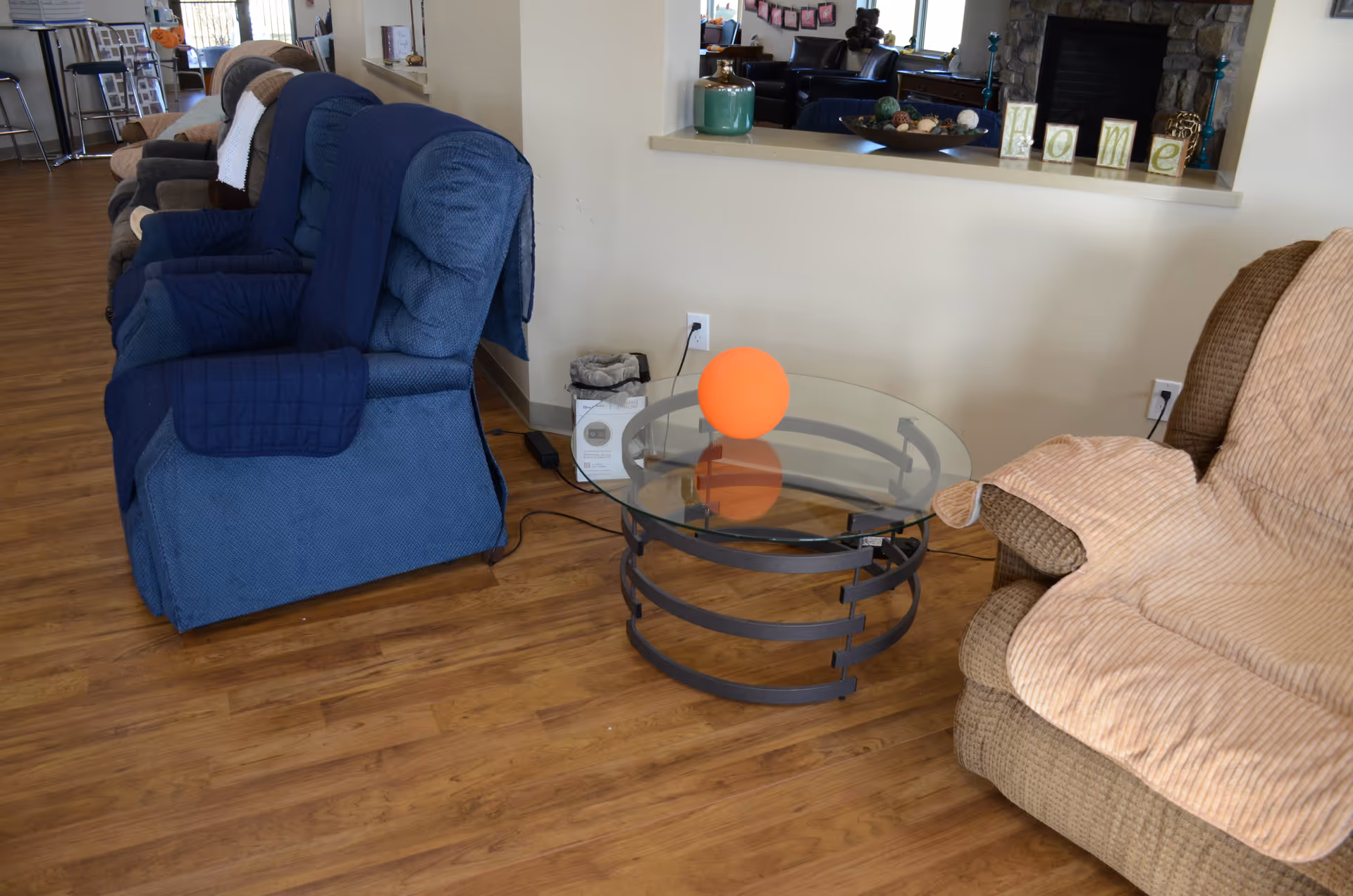 Blue recliners along a wall with an orange ball on a glass coffee table.