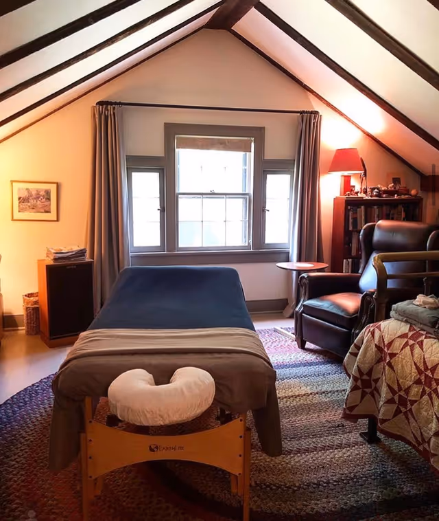 Cozy bedroom in a senior facility featuring a bed, window, armchair, and side table.