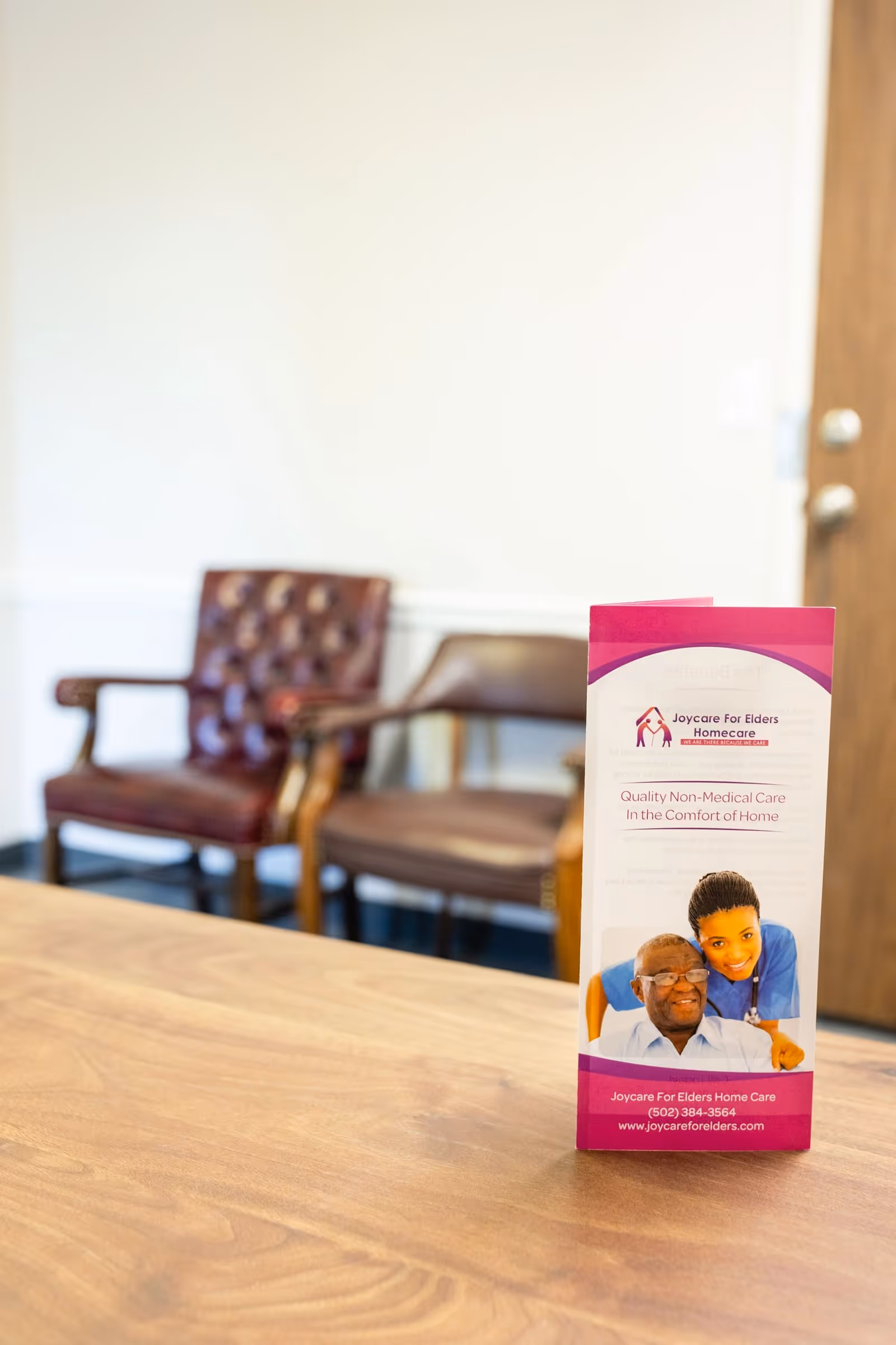 Boxed brochure on a wooden table in a reception area with brown chairs.