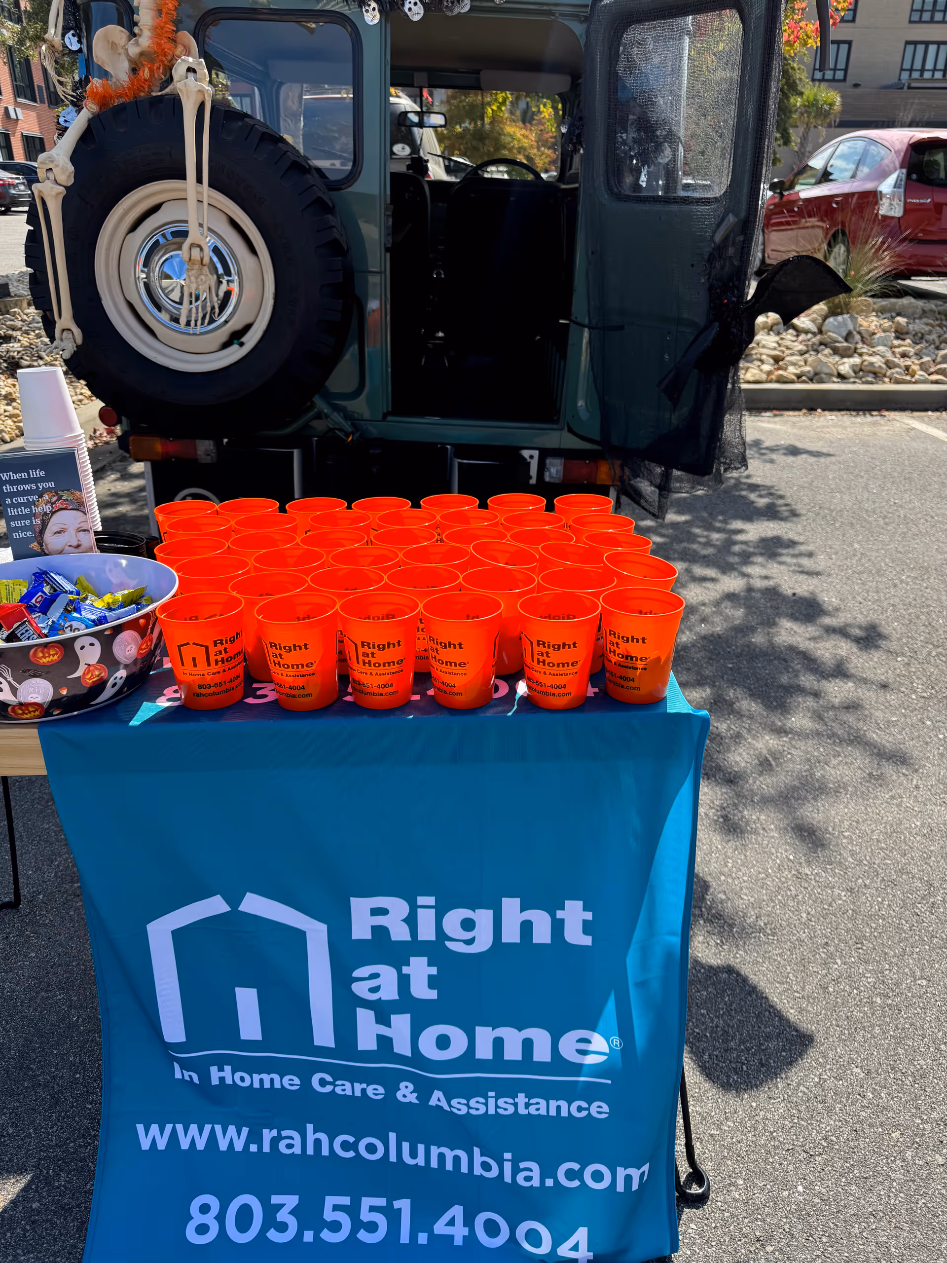 Outdoor promotional table with orange cups and Right at Home banner in a parking lot