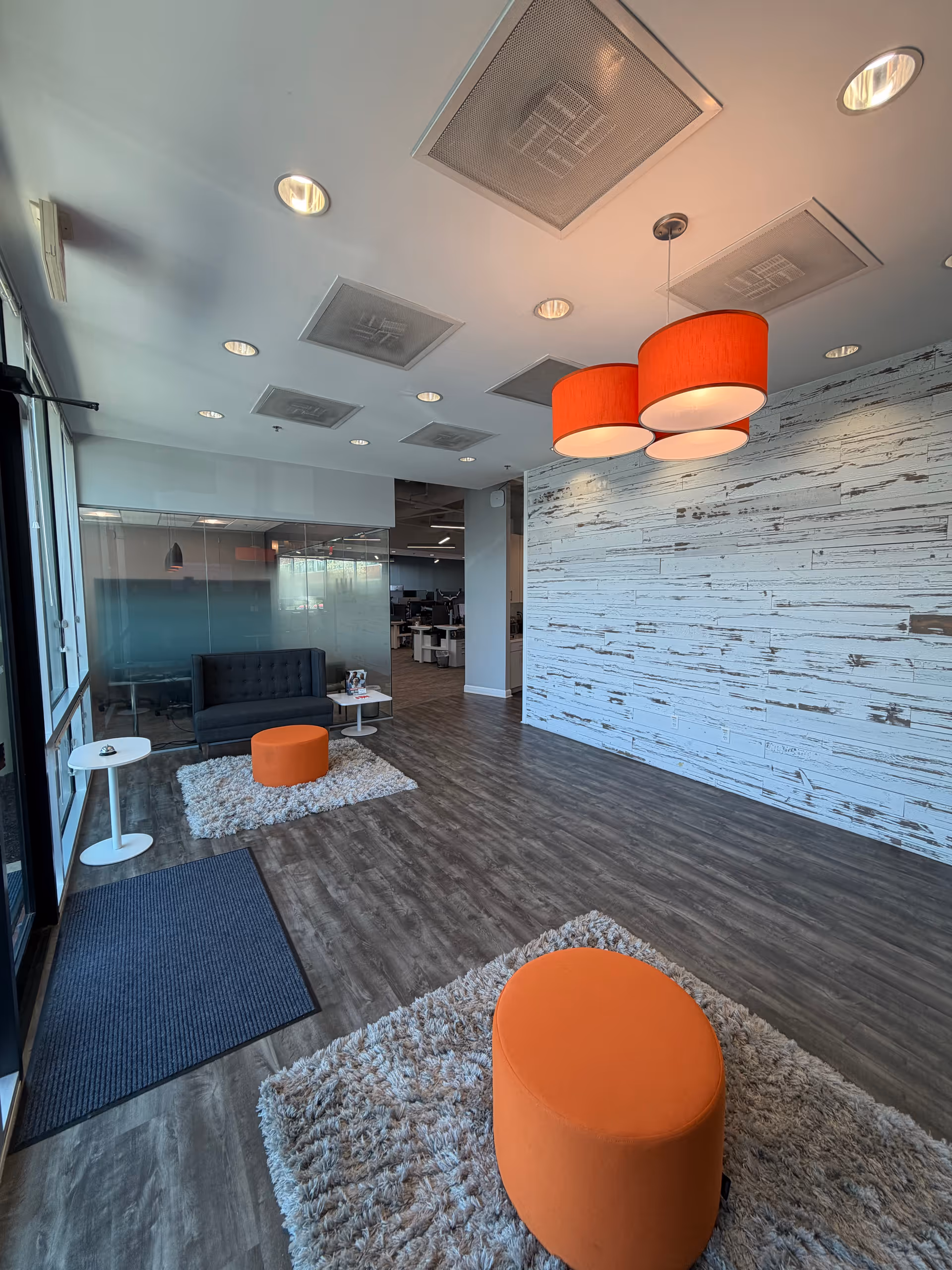 Modern senior living lounge with orange ottomans, plush rugs, and a glass partition.