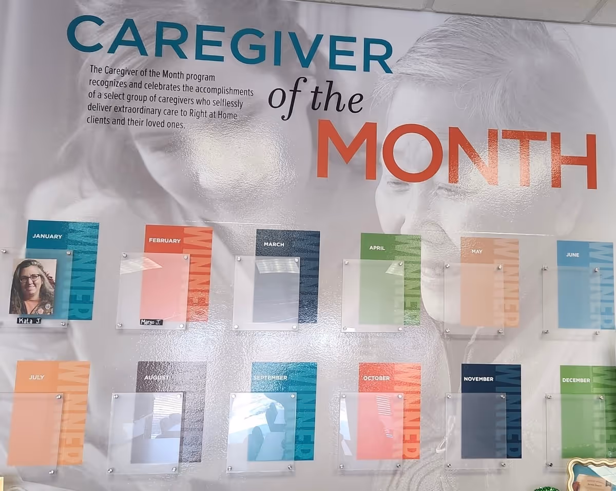 Indoor wall display titled Caregiver of the Month featuring monthly cards and photos.