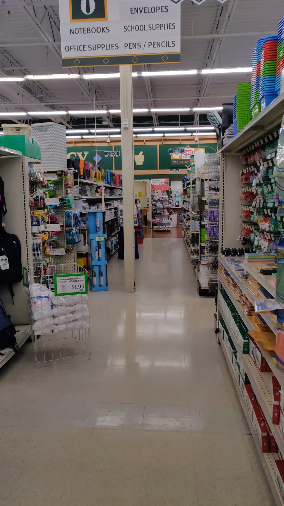 A wide store aisle with tall shelves stocked with various items and signs overhead.