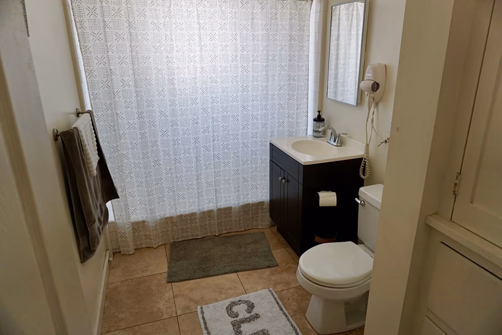 Compact bathroom featuring sink vanity, toilet, mirror, towels, and a patterned shower curtain.