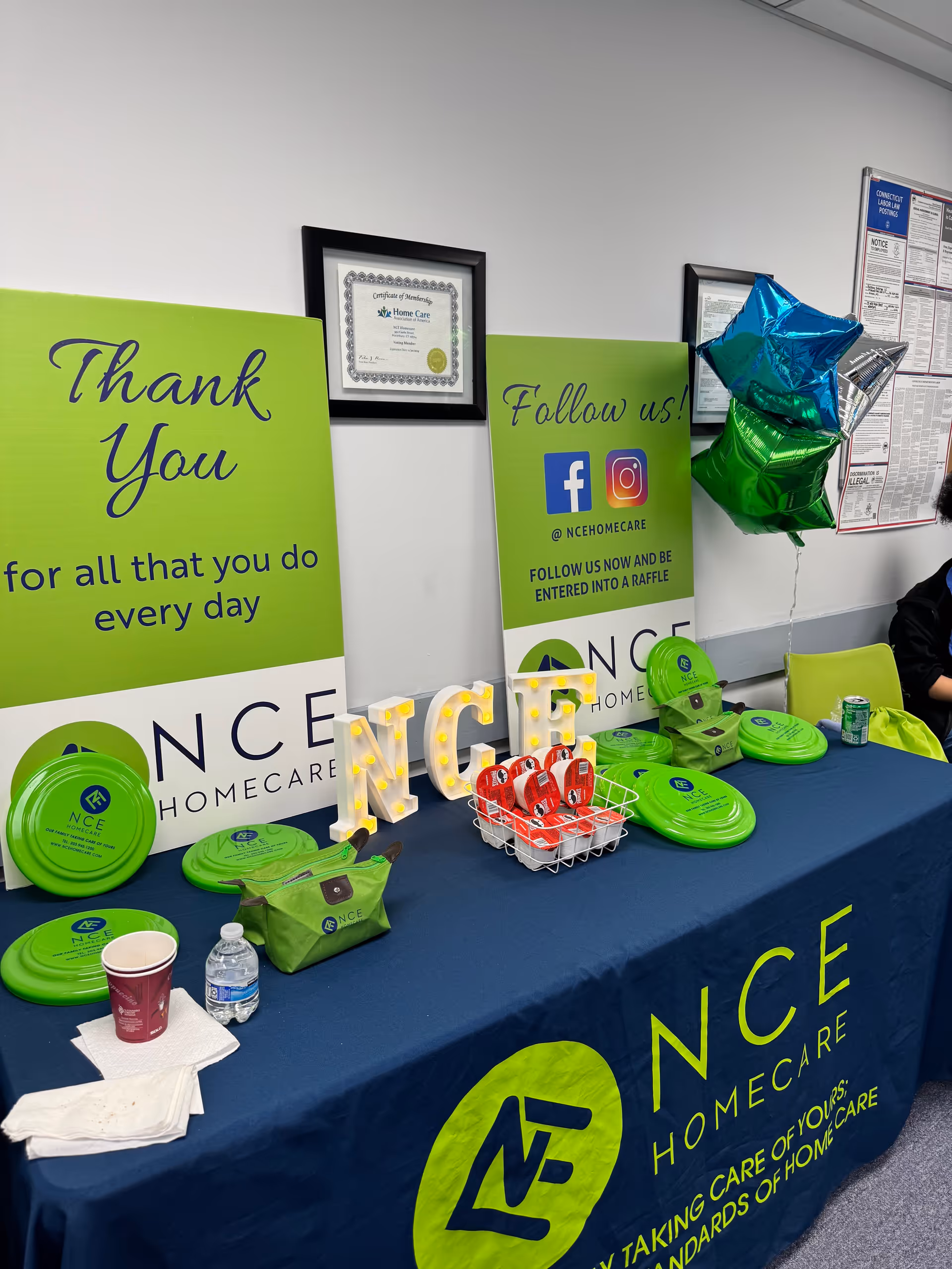 Promotional display table for NCE Homecare with green banners and signage.