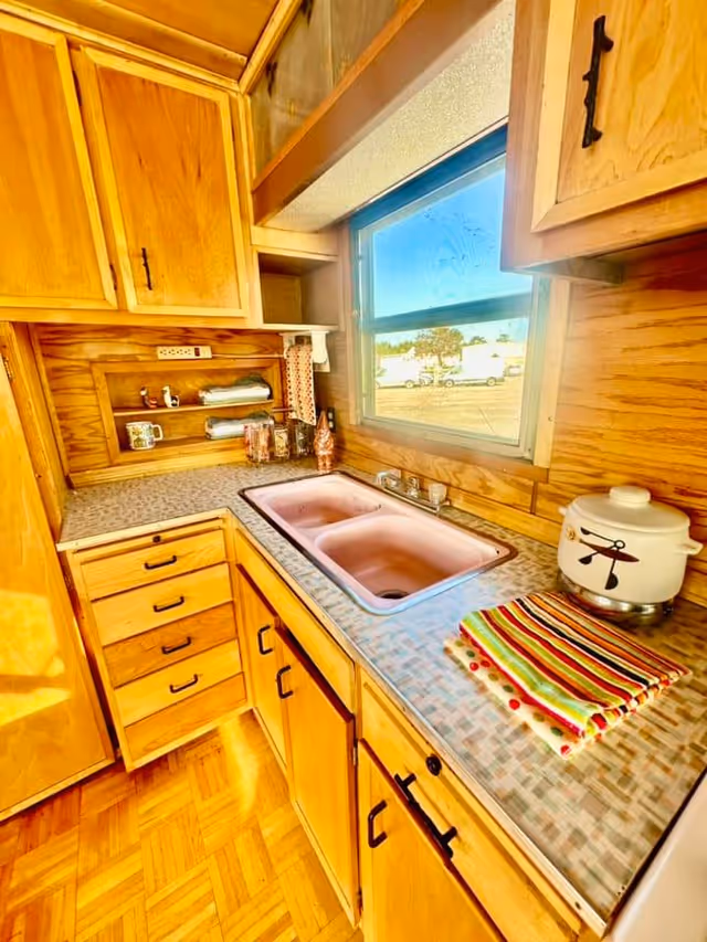 Wooden kitchen with double sink, ample counter space, and a window looking outside.
