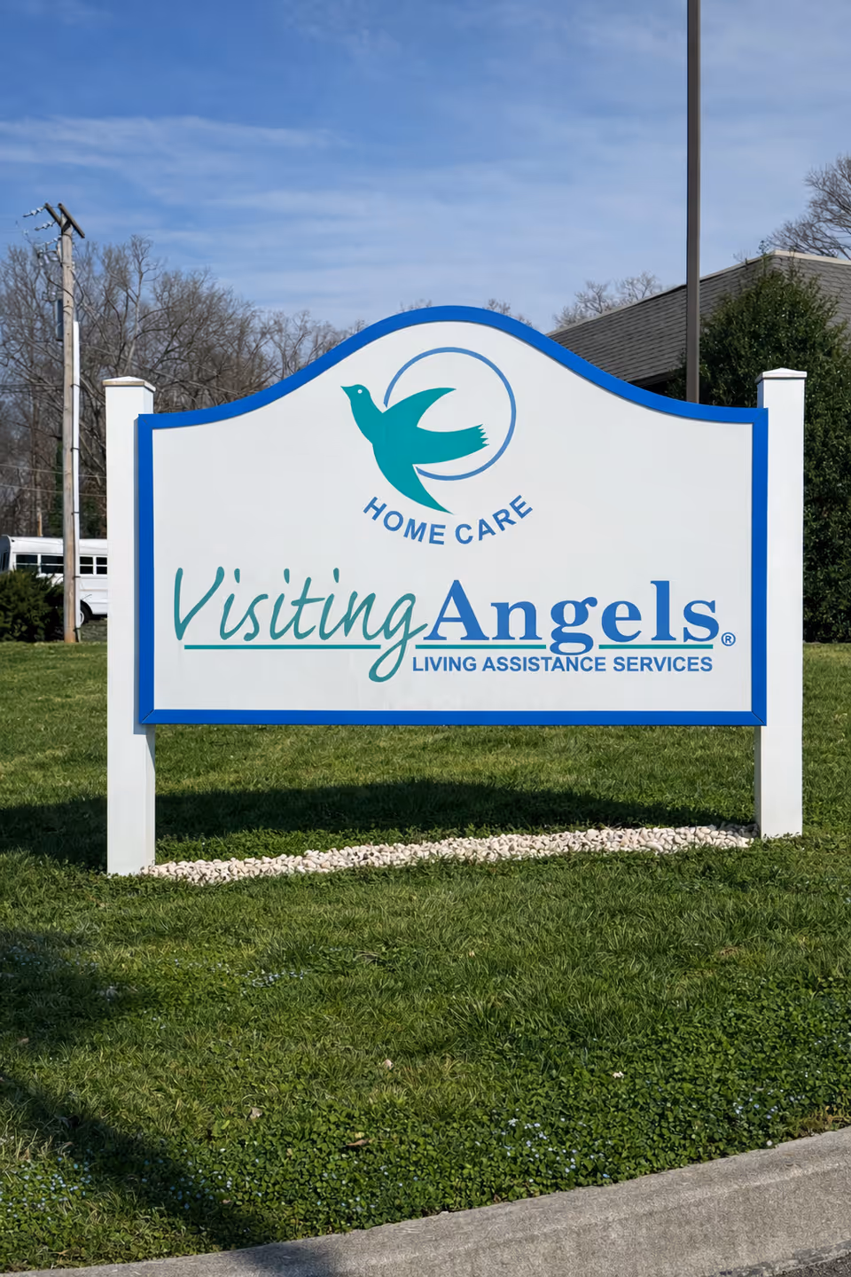 Large Visiting Angels sign with logo on a grassy front lawn by a building.