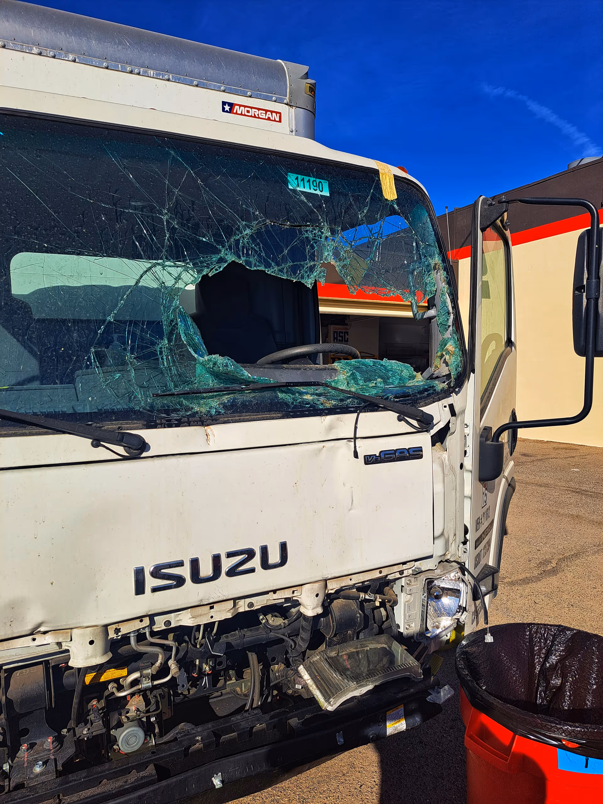 Front view of a white Isuzu bus with a shattered windshield and damaged front