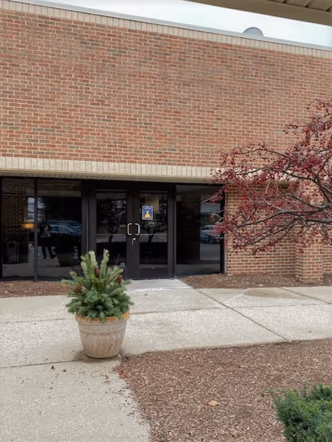 Brick exterior building entrance with glass doors and a potted plant.
