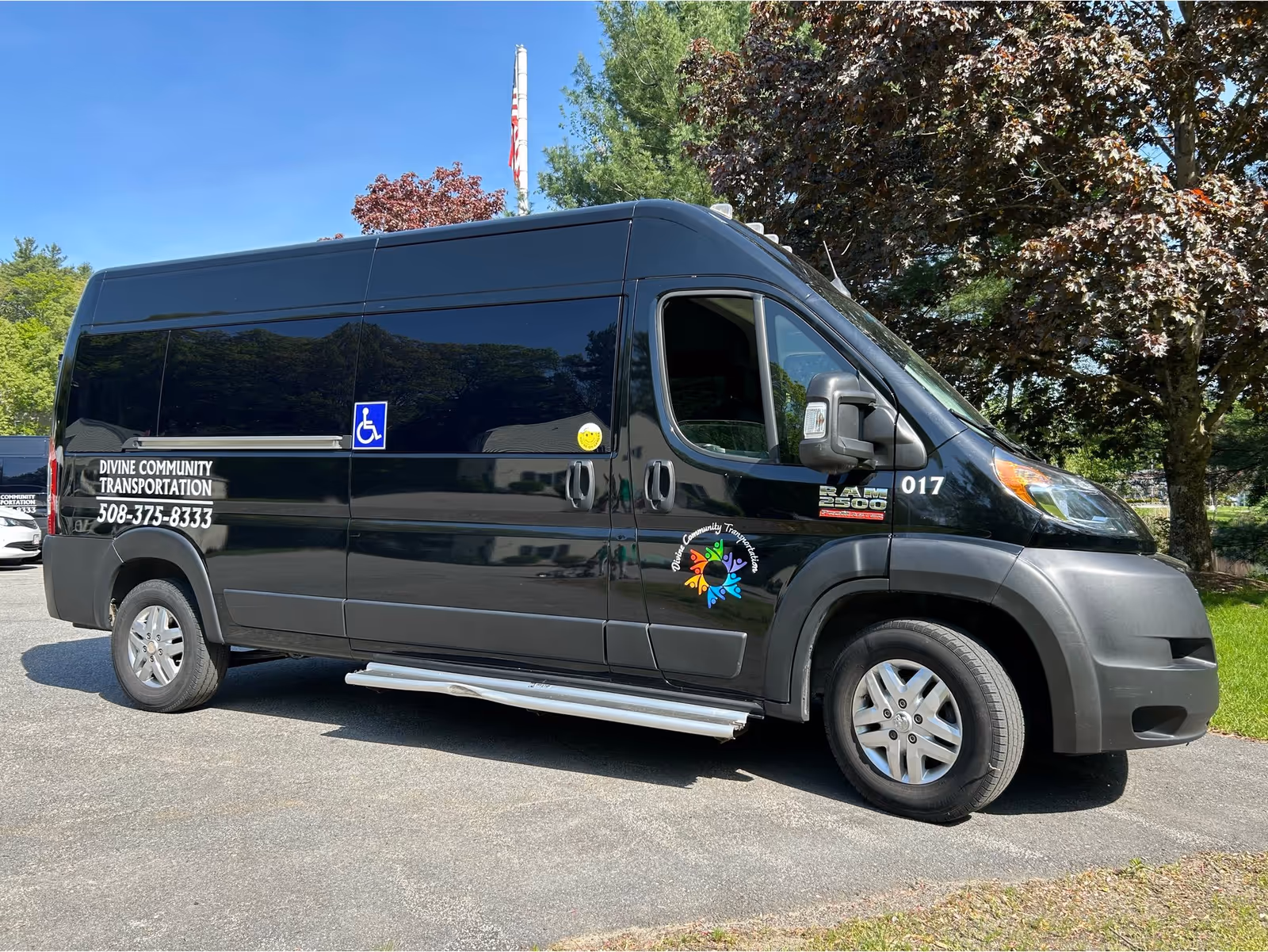Black van labeled Divine Community Transportation parked in a parking lot beside trees.