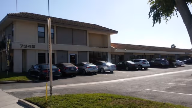 Front exterior of a beige building with a row of parked cars