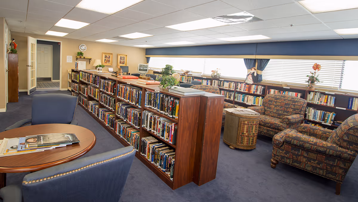 Interior library lounge with bookshelves, comfortable seating, and sunlit windows.