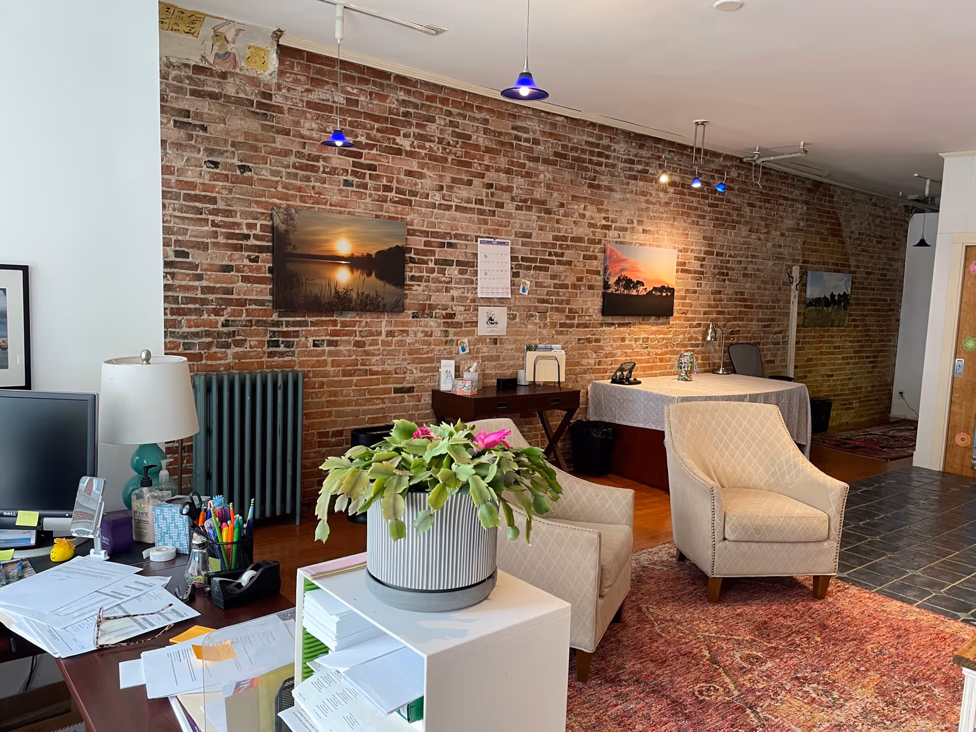 Brick-walled lobby with seating, desks, plants, and artwork in a senior living facility.