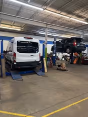 Inside MobilityWorks facility, a white van on a lift beside a black SUV on another lift.