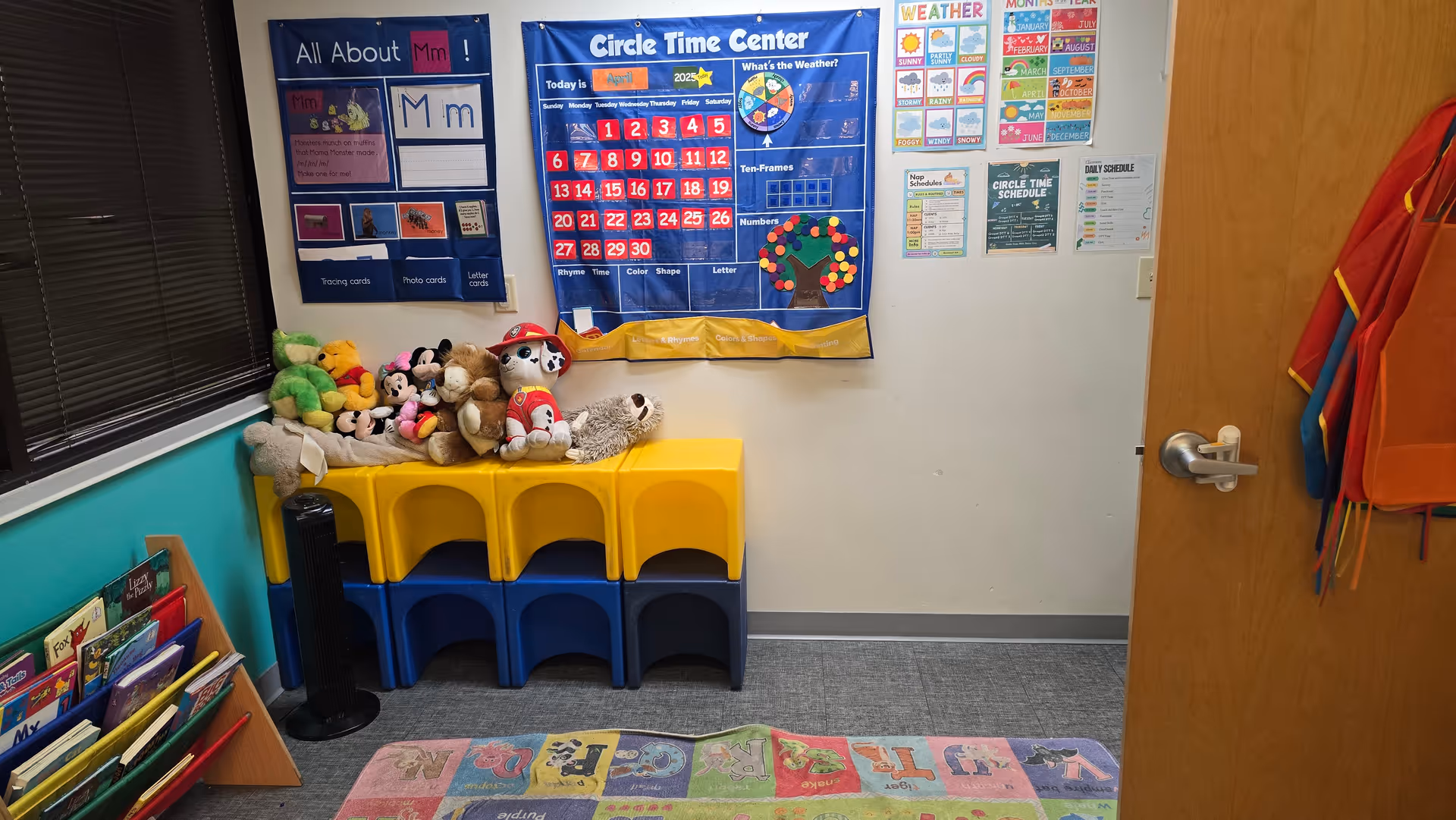 Bright classroom corner with stuffed animals, colorful stackable chairs, posters, and a door.