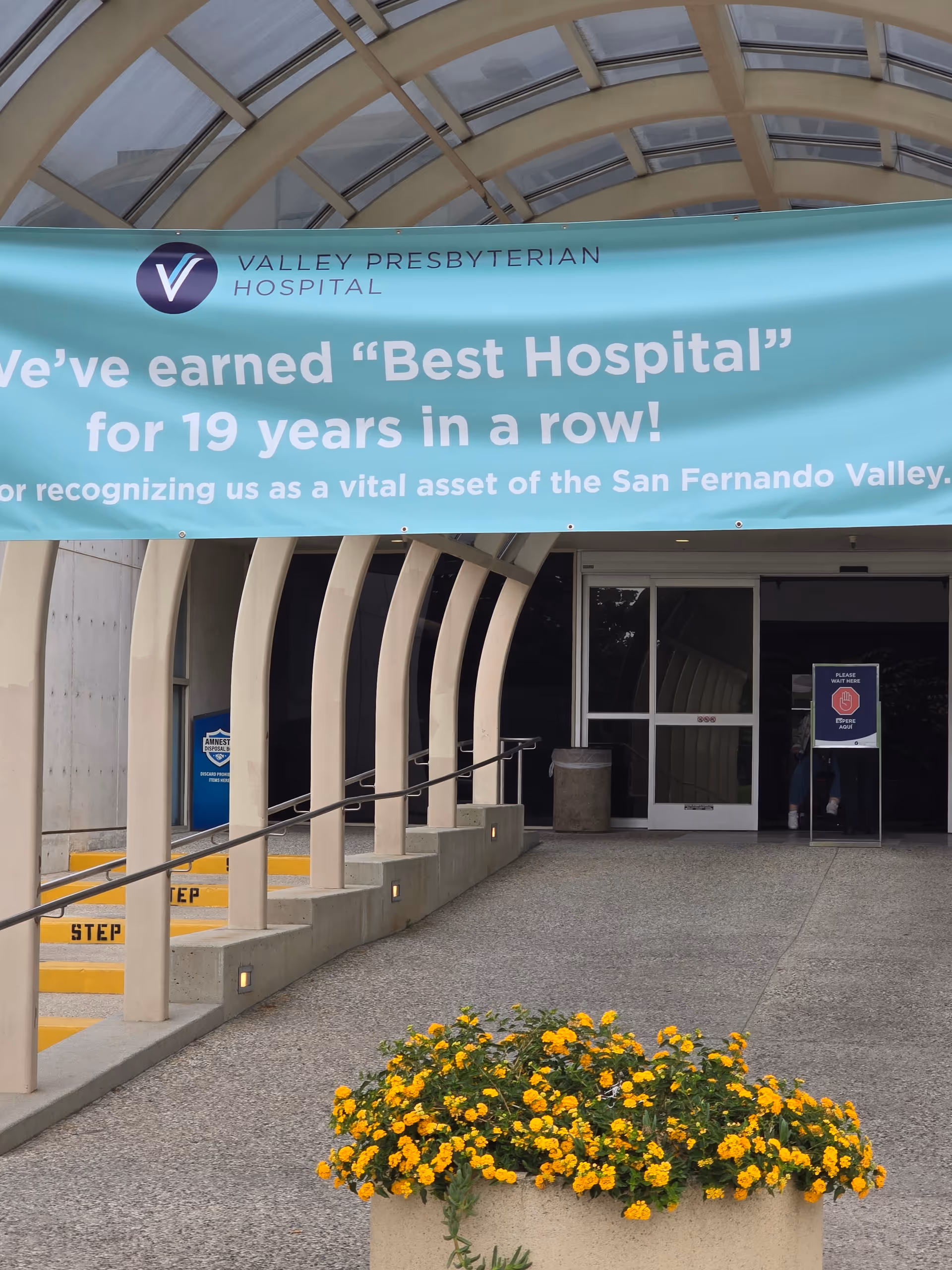 Hospital entrance with turquoise banner, curved arches, and yellow flowers in the foreground.