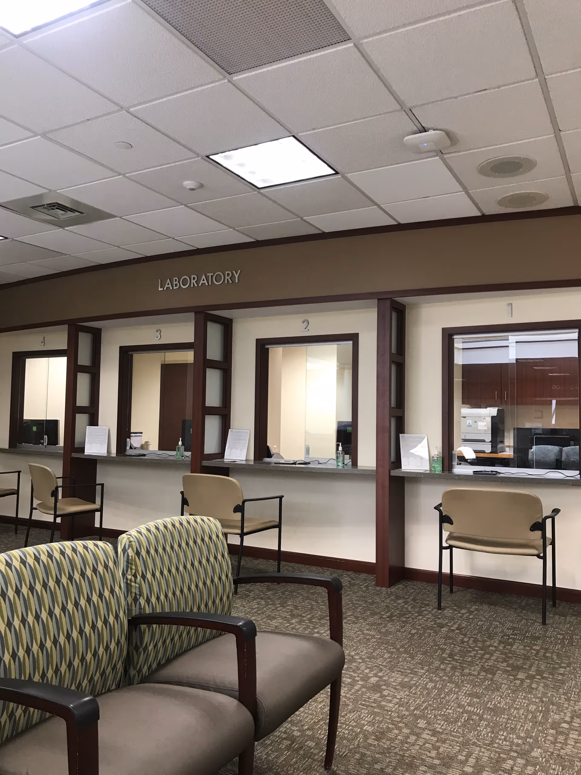 Interior view of a hospital-like waiting area with laboratory service windows and chairs.