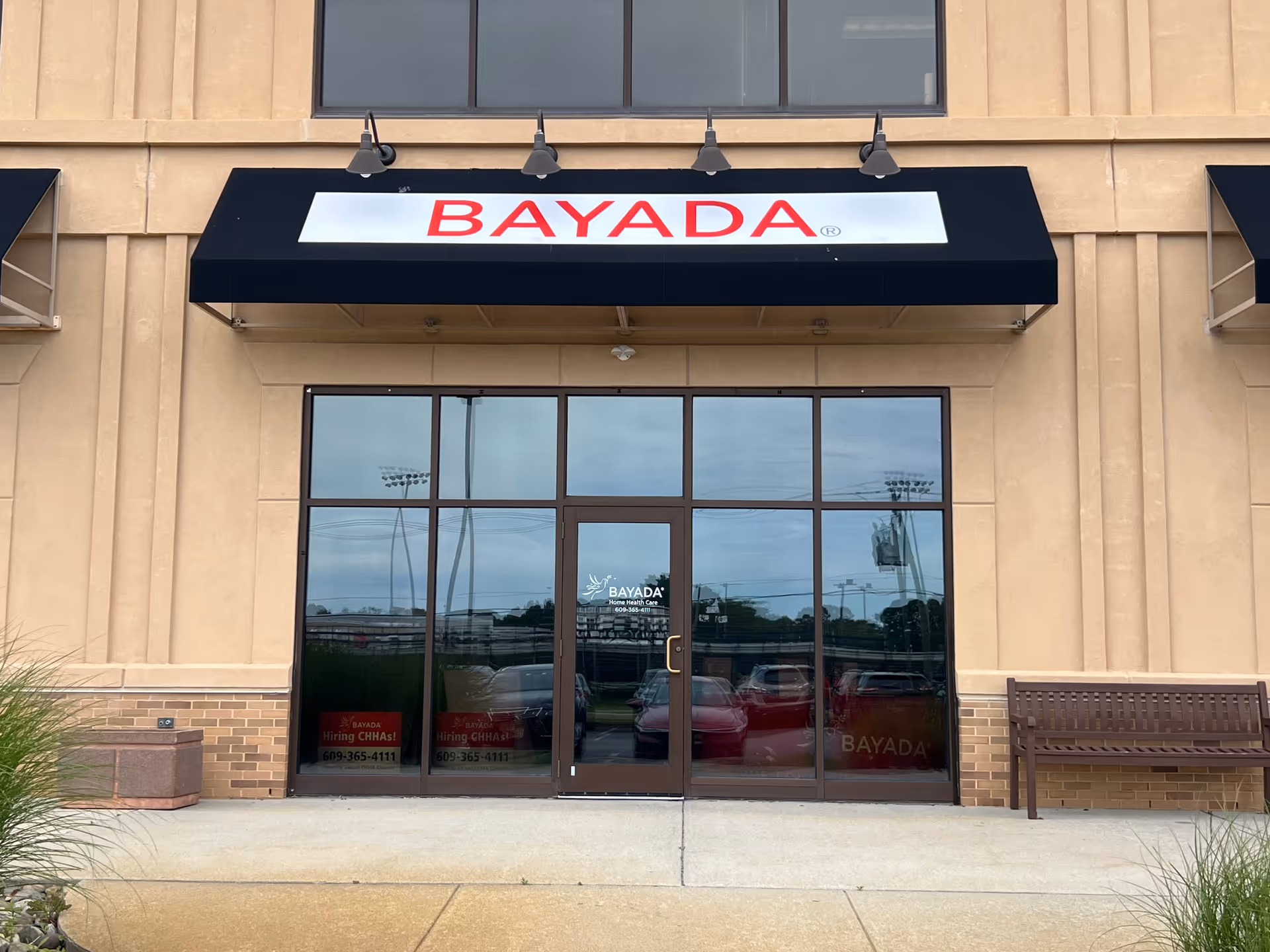 Exterior view of BAYADA Assistive Care storefront with glass doors and a bench outside.