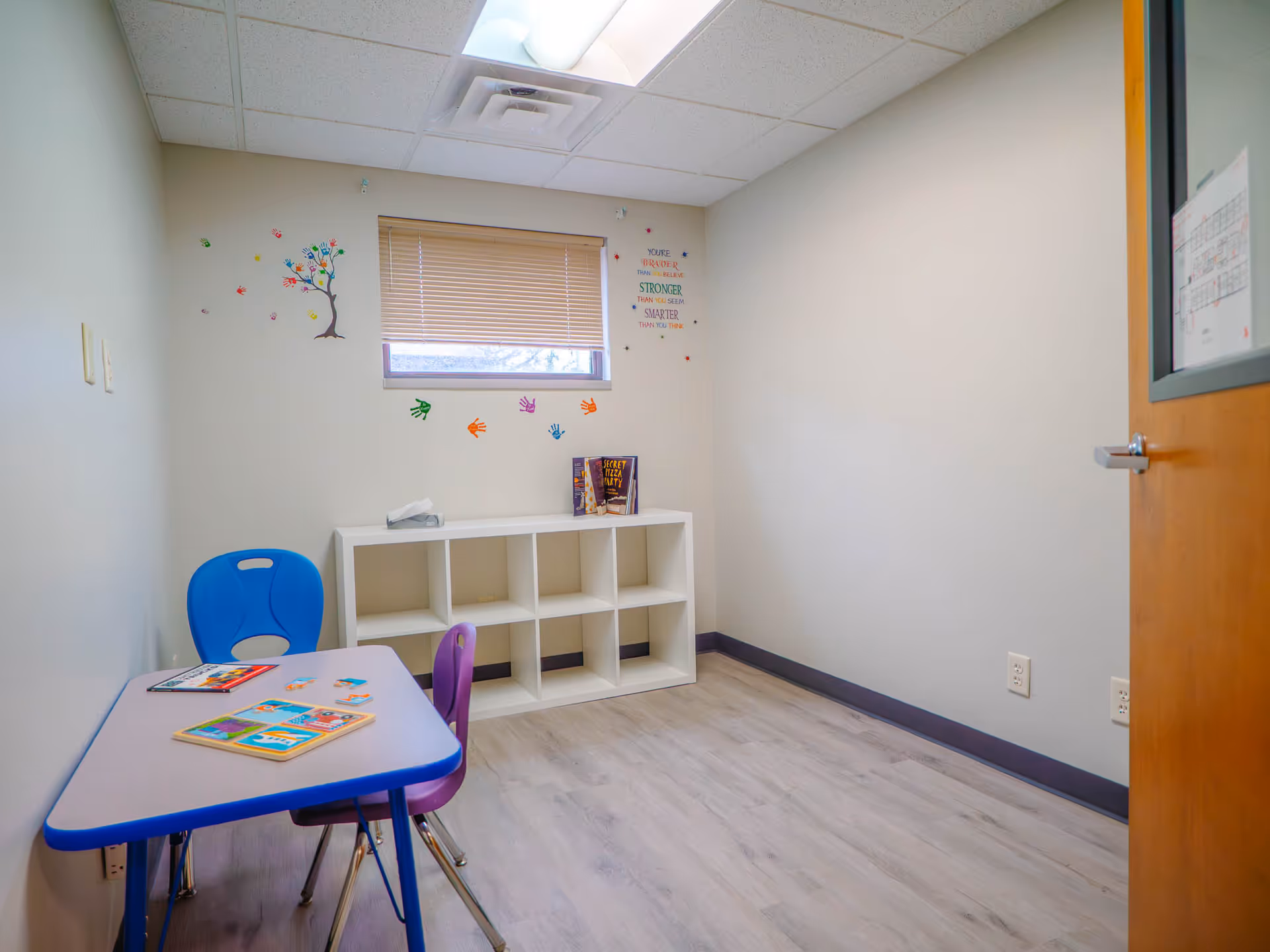 Small children's activity room with a blue table, chairs, cubbies, and wall decals.