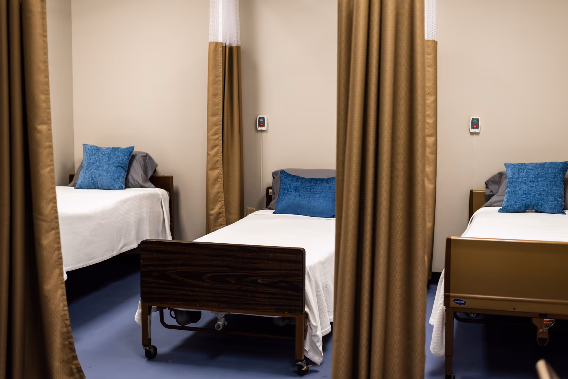 Three hospital beds separated by curtains in a small private care ward.