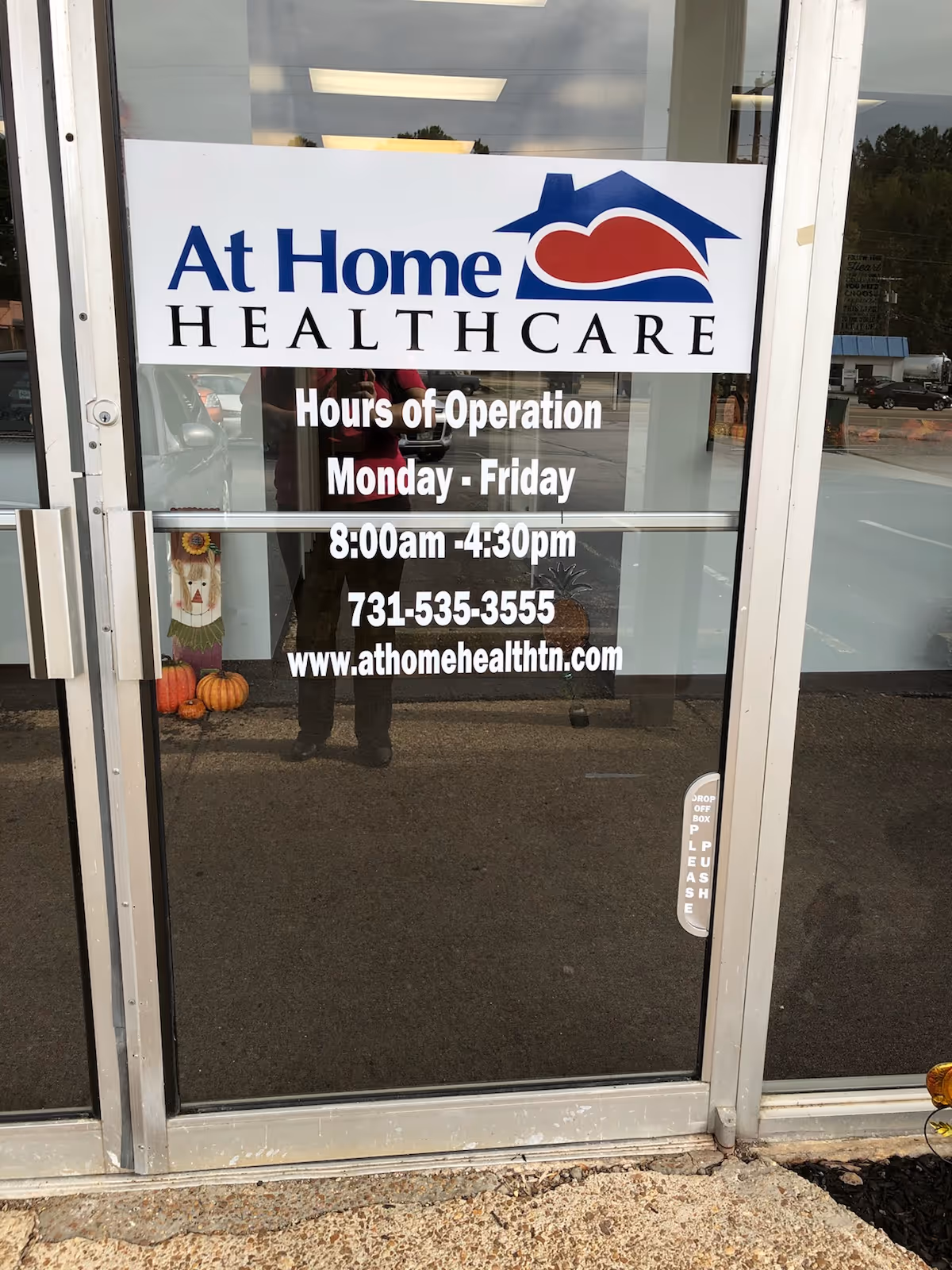 Front glass door displaying At Home Healthcare sign and hours