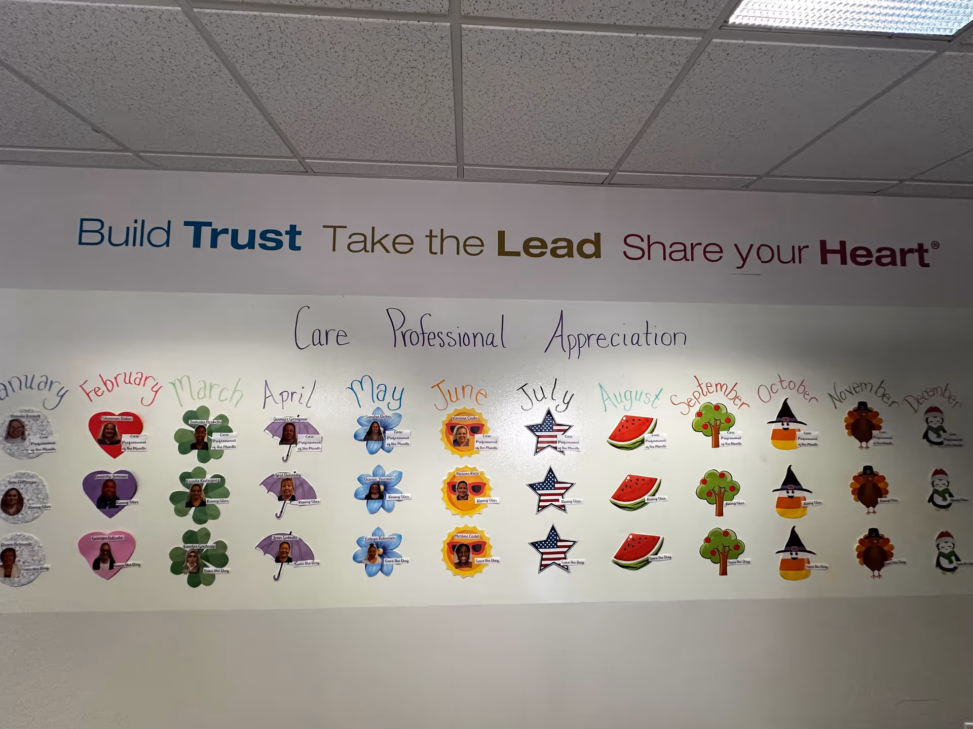 Indoor wall display with a Build Trust banner and monthly caregiver recognition decorations.