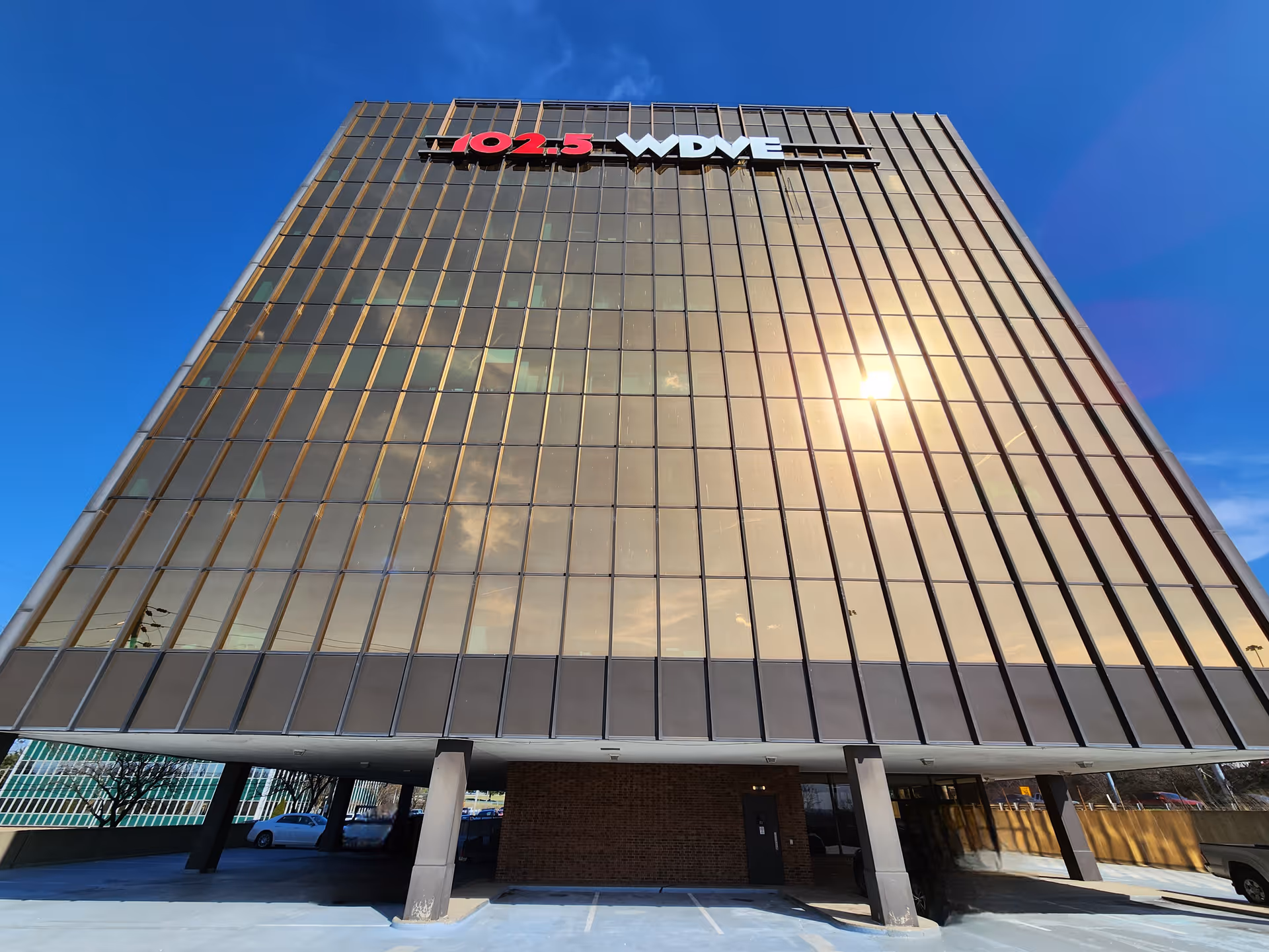 Tall glass-front office building with a 102.5 WDVE sign and parking below.