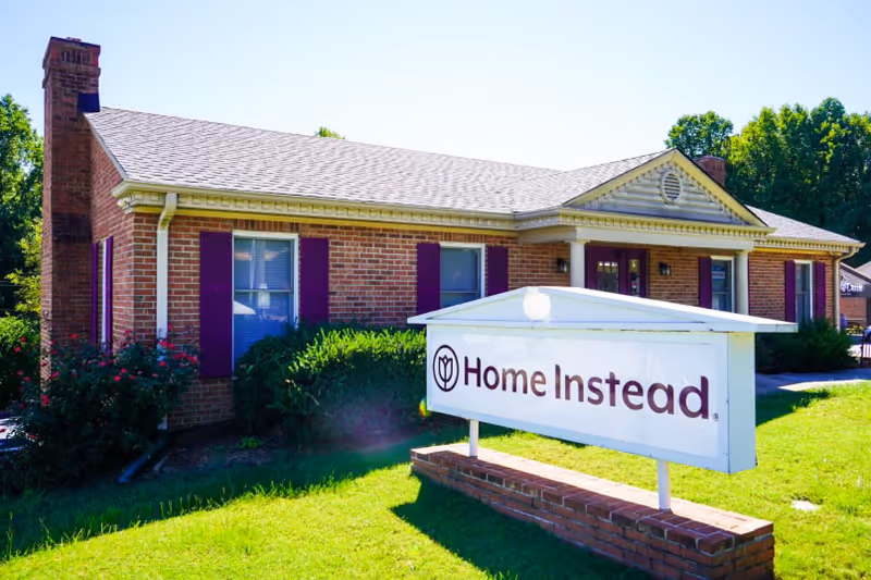 Brick, single-story Home Instead building with a sign in the neatly landscaped front lawn.