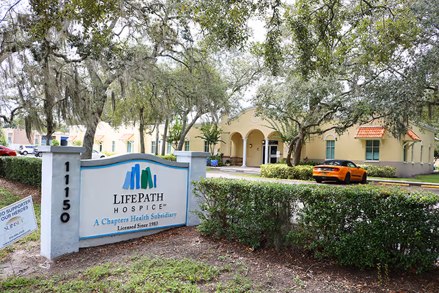 Exterior view of Lifepath Hospice building with sign, manicured hedges, and a parked orange car.