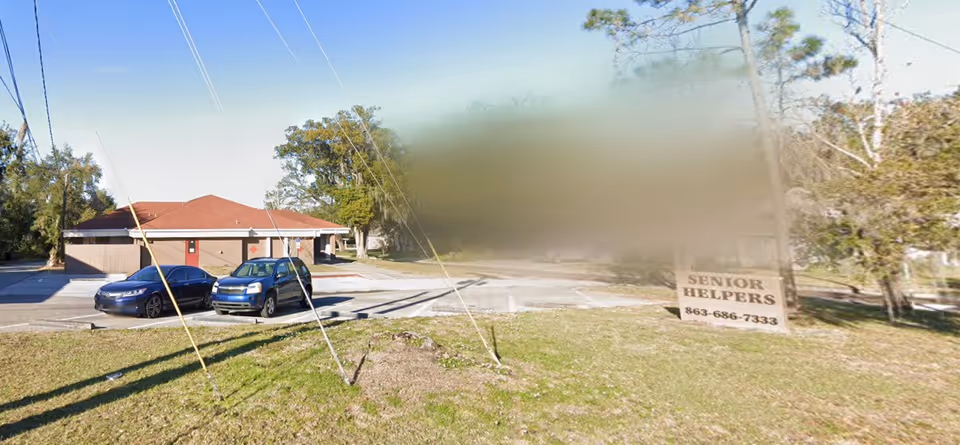 Exterior view of a Senior Helpers facility with a lawn sign and parked cars.