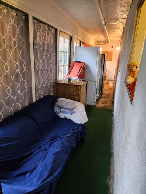 Narrow indoor corridor with a blue sofa, patterned curtains, and a teddy bear on a shelf.