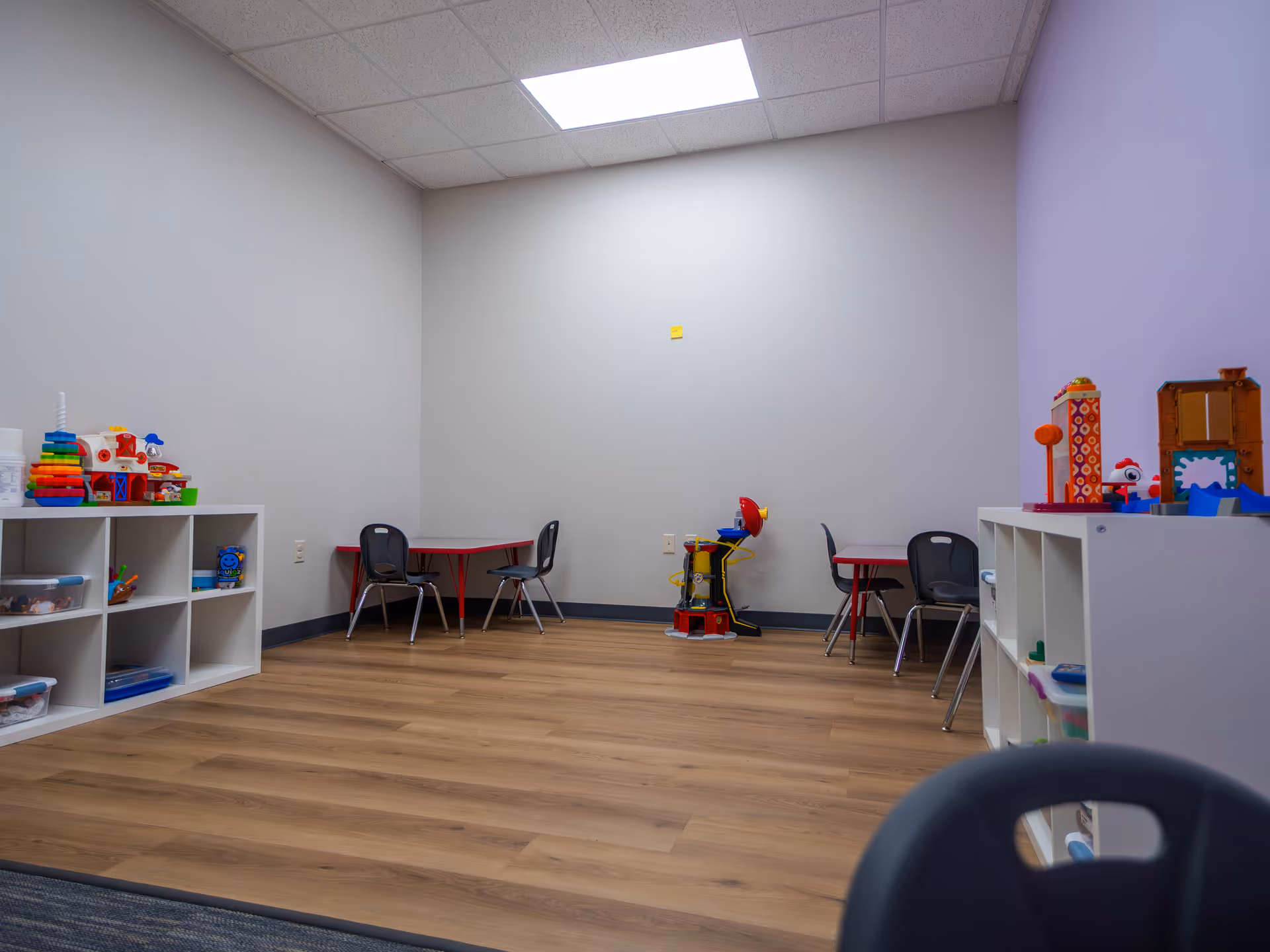 Bright children's playroom with toy shelves, tables, and small chairs in a colorful room.